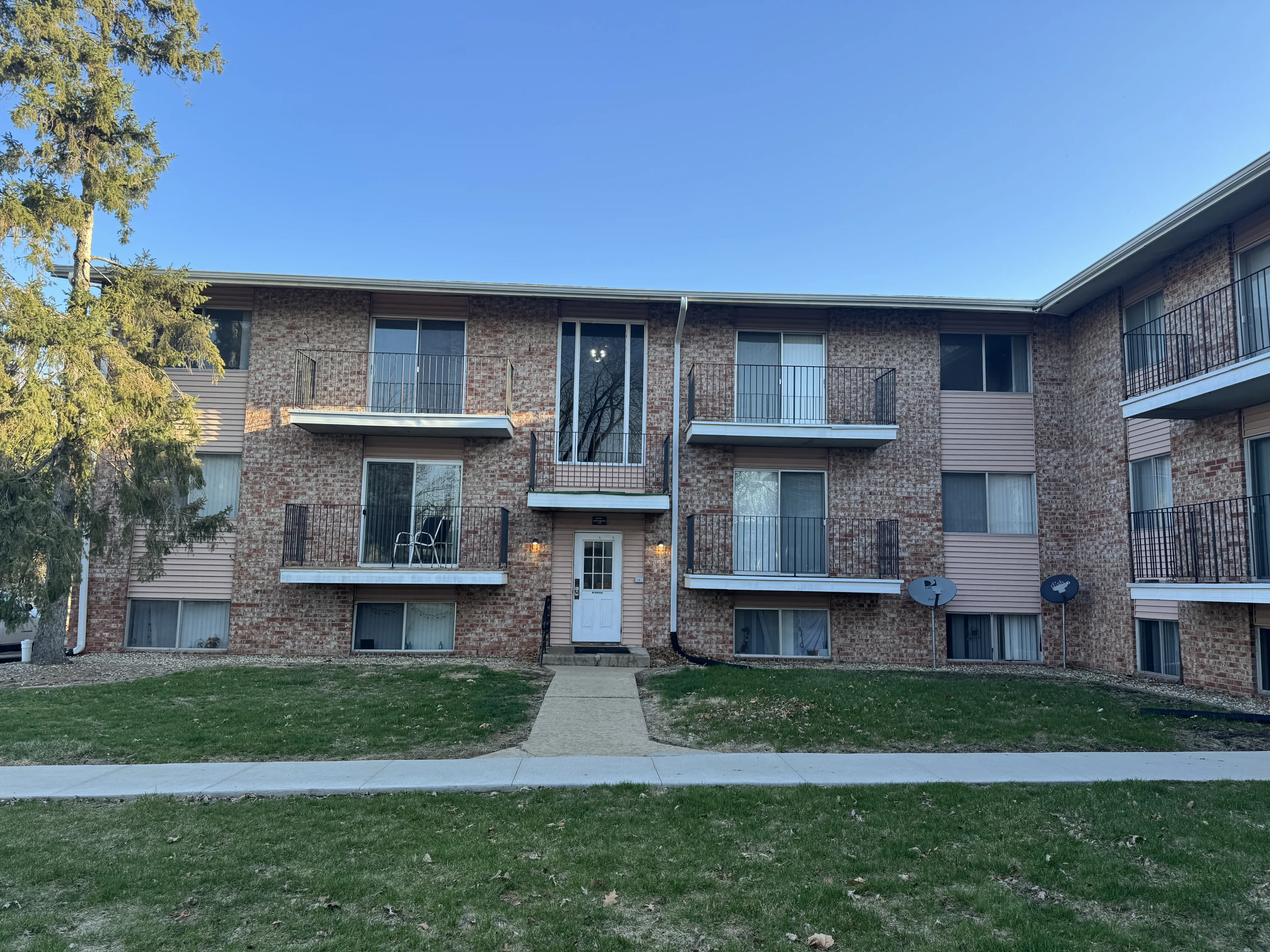 Charming brick apartment building with balconies and lush green lawn, offering a cozy residential atmosphere.