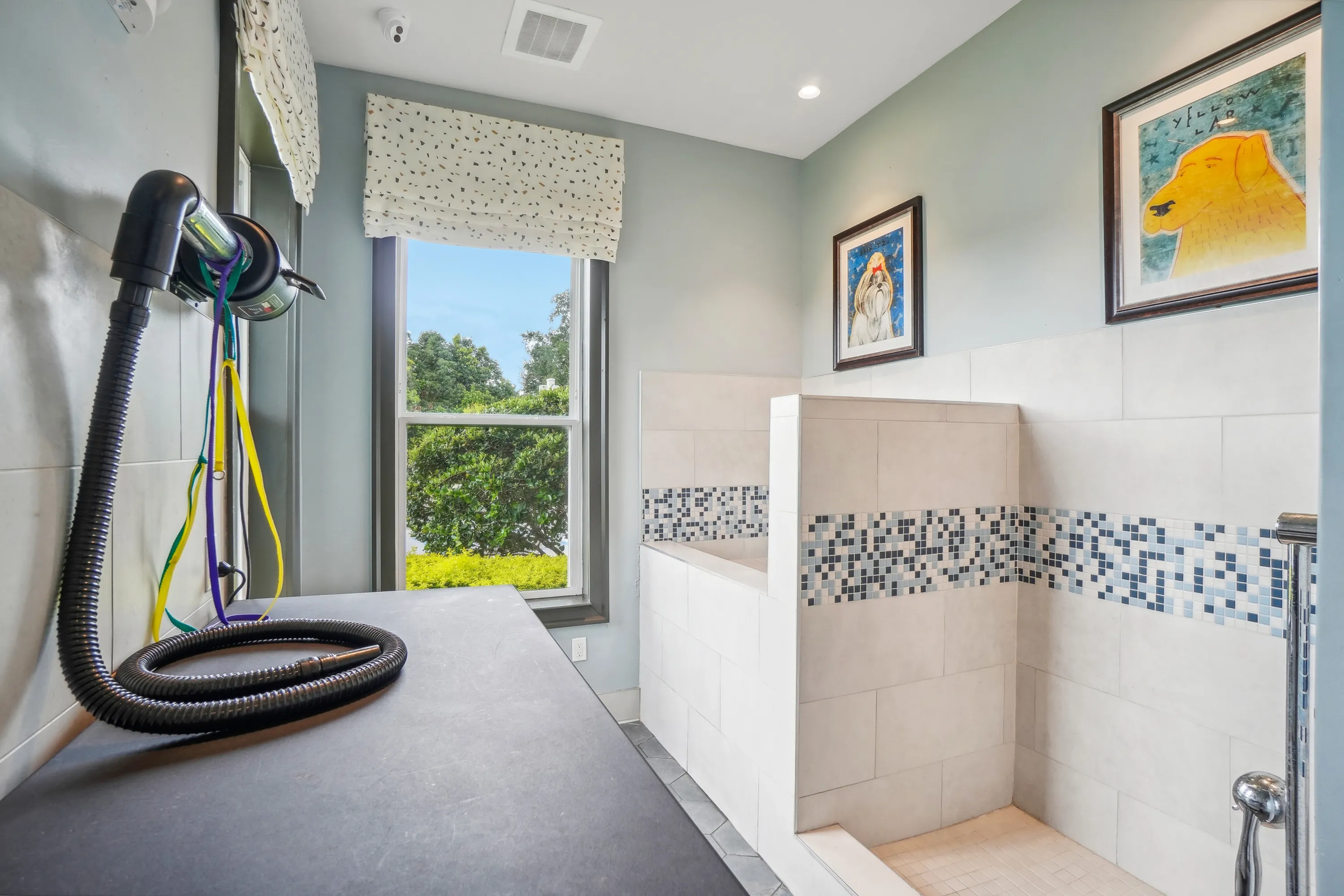 Bright and modern bathroom with chic mosaic tile accents, large window with lush garden view, and artistic wall decor.