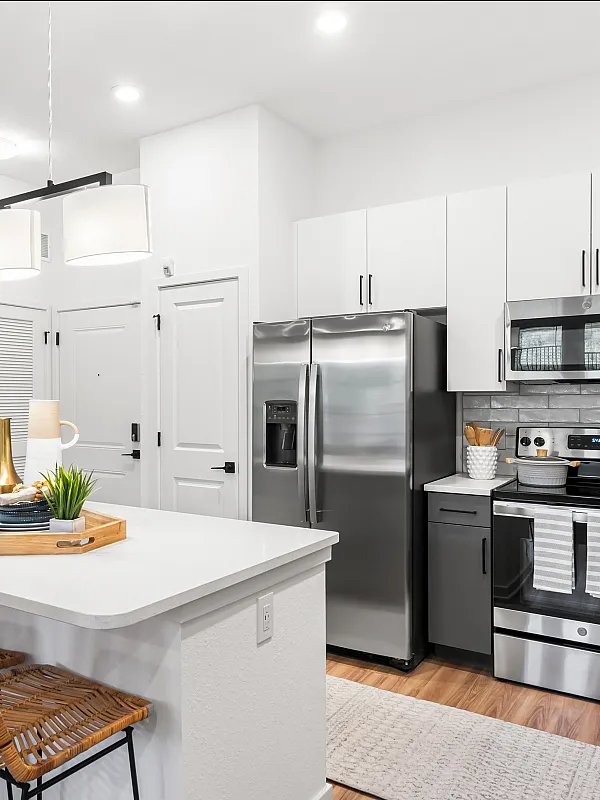 Modern kitchen with sleek stainless steel appliances, elegant white countertops, and stylish wicker bar stools, perfect for contemporary living.