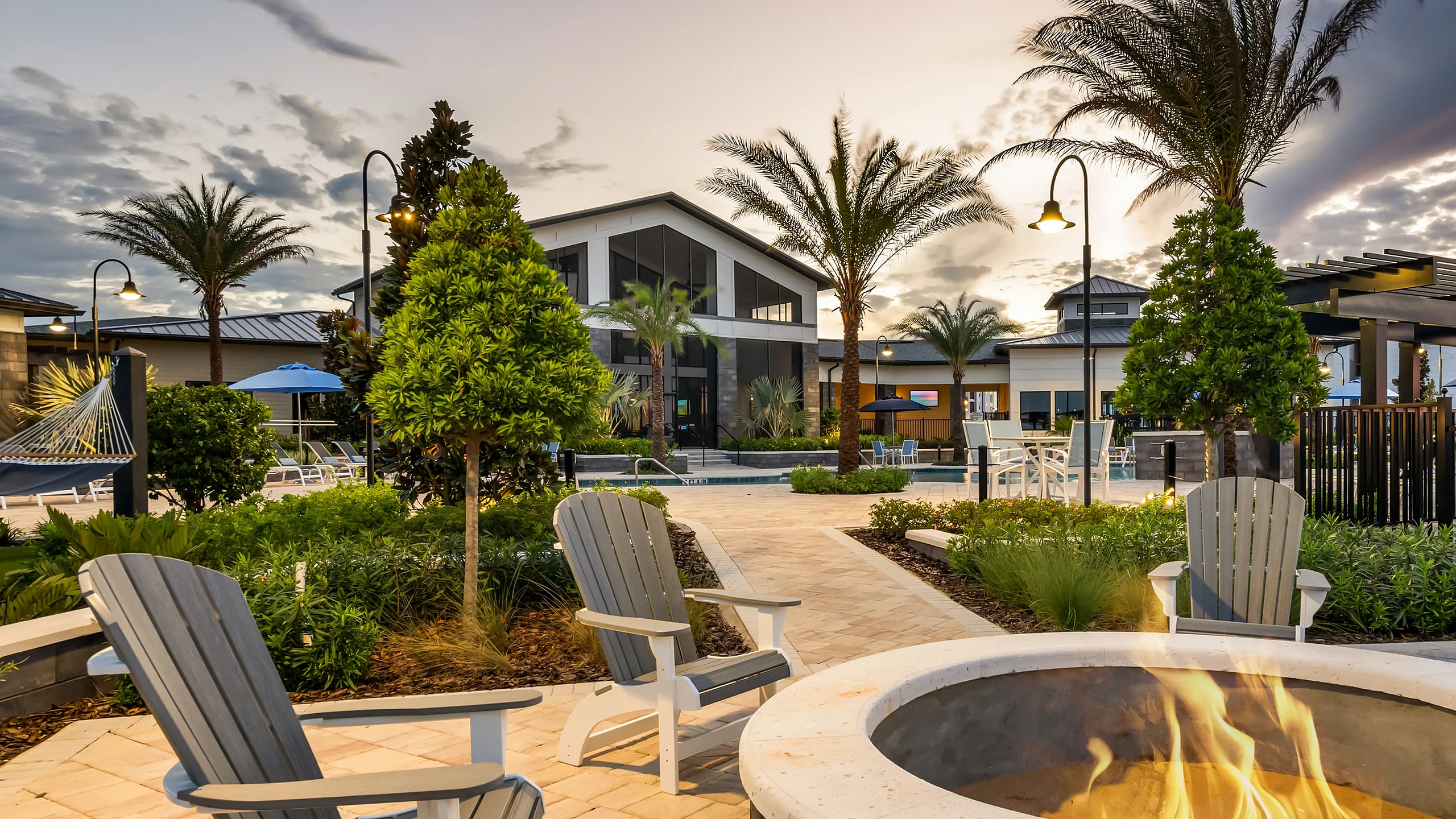 Inviting outdoor lounge area with cozy fire pit, surrounded by lush greenery and palm trees at sunset, perfect for relaxation.