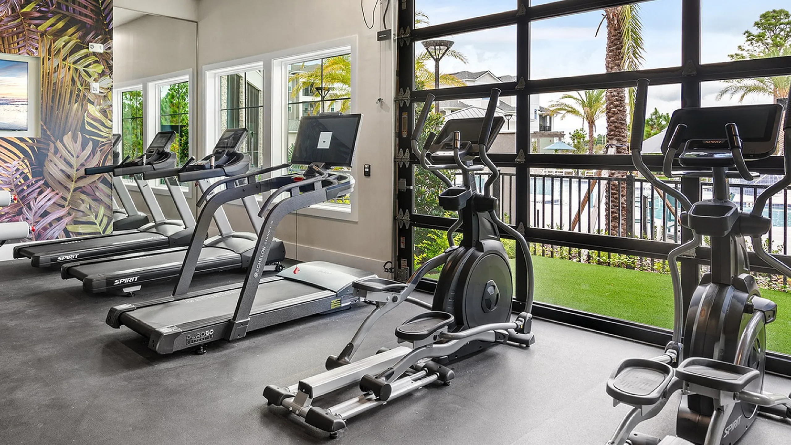 Modern gym with state-of-the-art equipment, vibrant wall art, and scenic outdoor views through large windows.