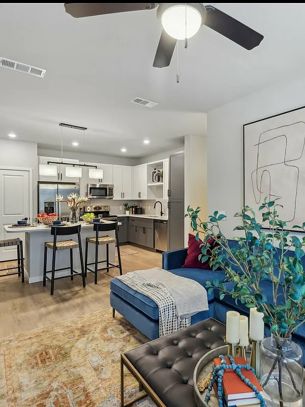 Modern open-concept living room and kitchen with chic decor, featuring a plush blue sofa, stylish artwork, and sleek kitchen island with bar stools.