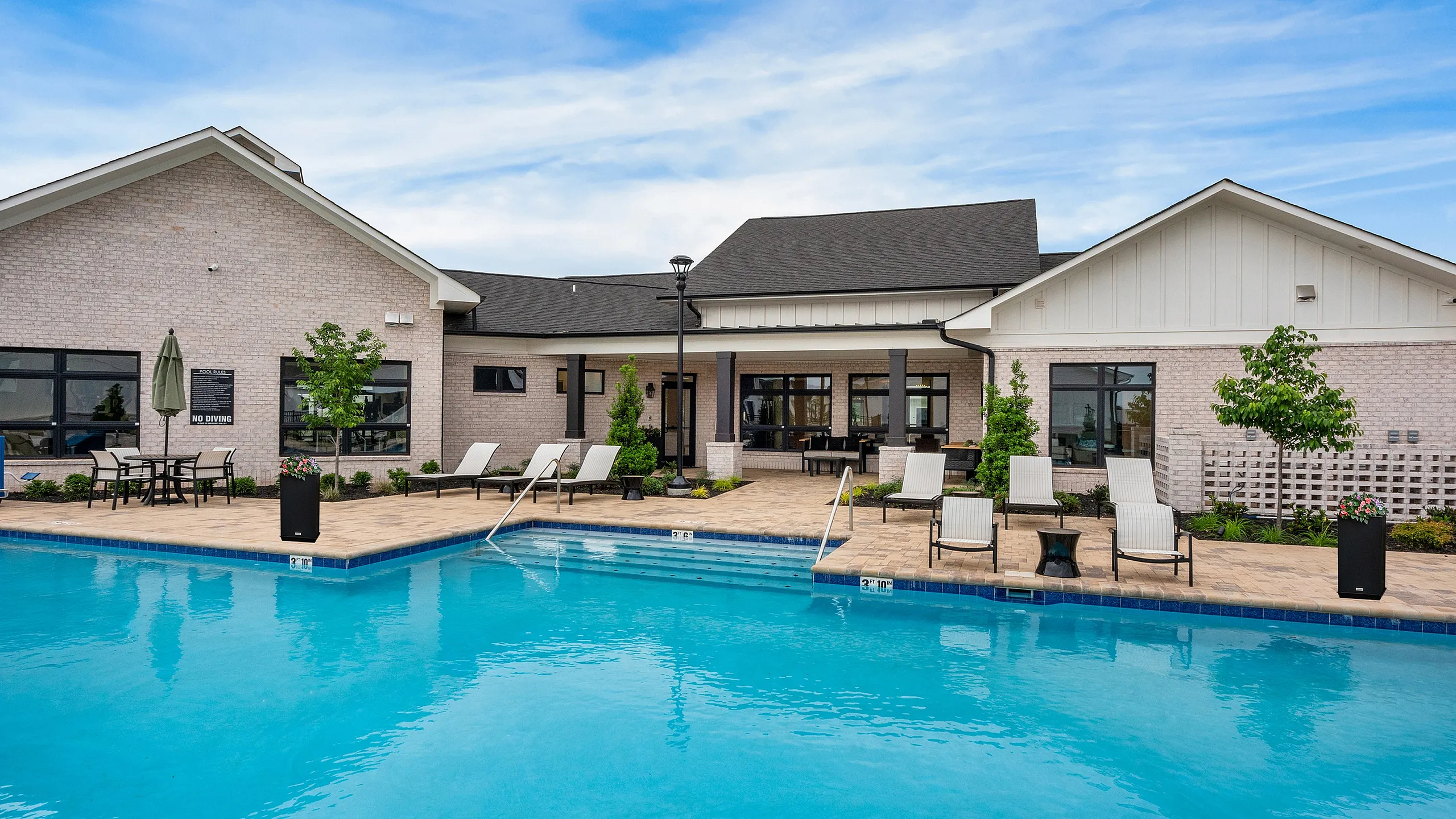 Luxurious apartment community featuring a stunning outdoor swimming pool surrounded by elegant lounge chairs and lush landscaping under a bright blue sky.