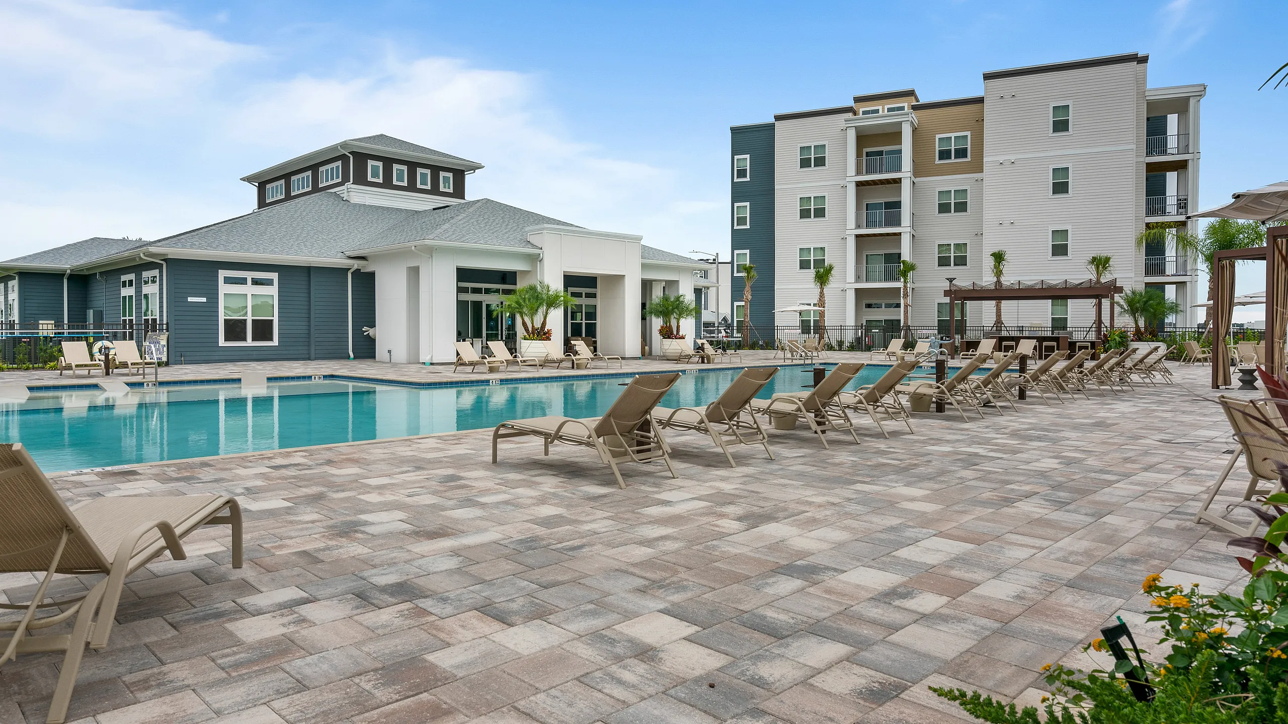 Luxury apartment complex with modern architecture, featuring a sparkling swimming pool, sun loungers, and vibrant landscaping.