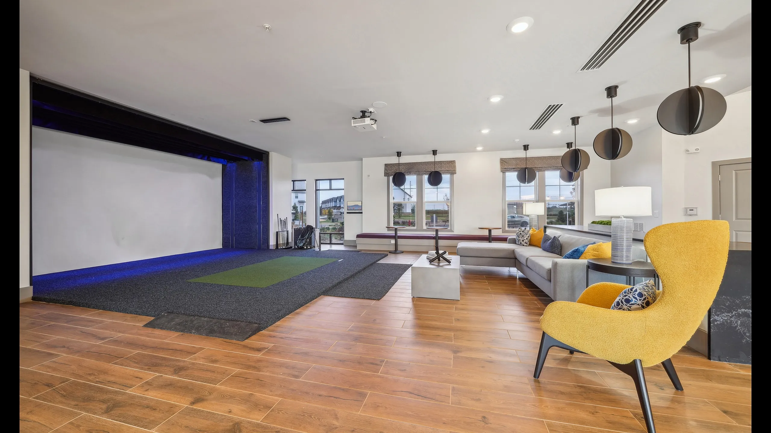 Spacious and modern lounge area with vibrant yellow seating, sleek wooden flooring, and an indoor golf simulator, perfect for luxury living.