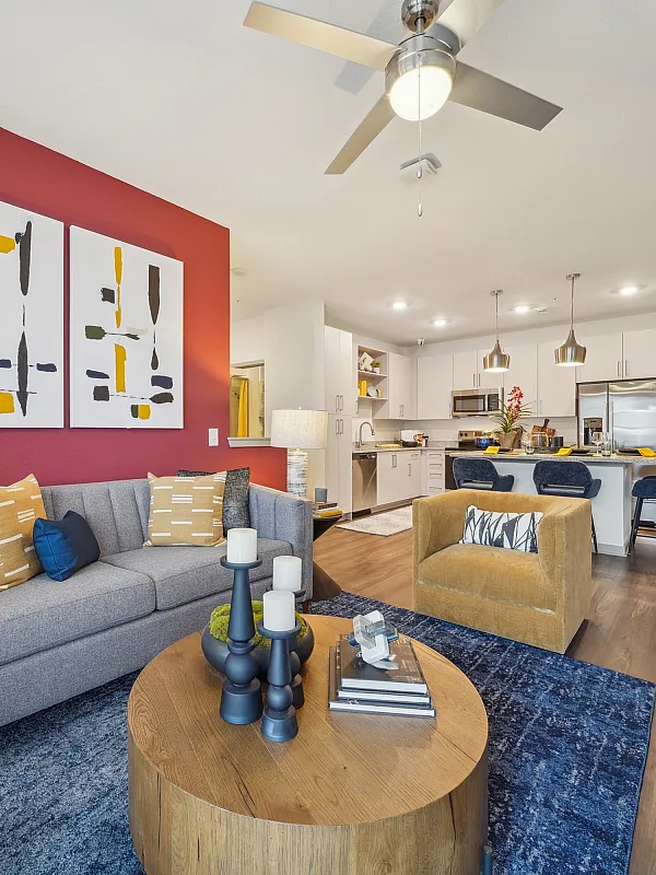 Modern living room with elegant decor, featuring a stylish grey sofa against a vibrant red accent wall, abstract artwork, cozy mustard armchair, and an open-concept kitchen with sleek appliances.