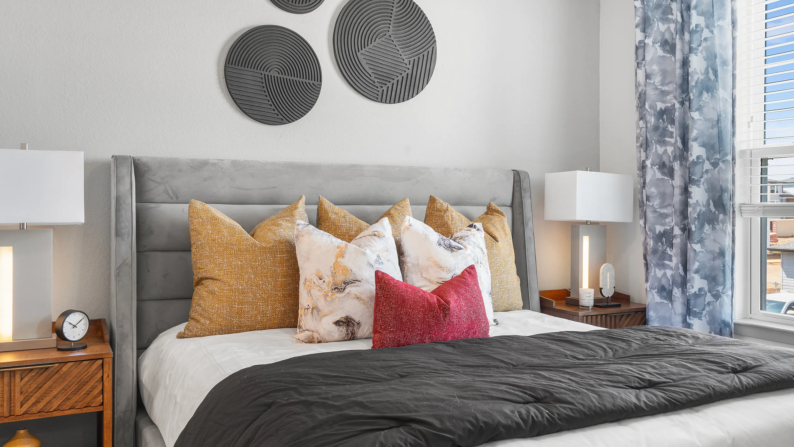 Chic bedroom with a plush gray headboard, vibrant throw pillows, modern bedside tables, and stylish wall decor.