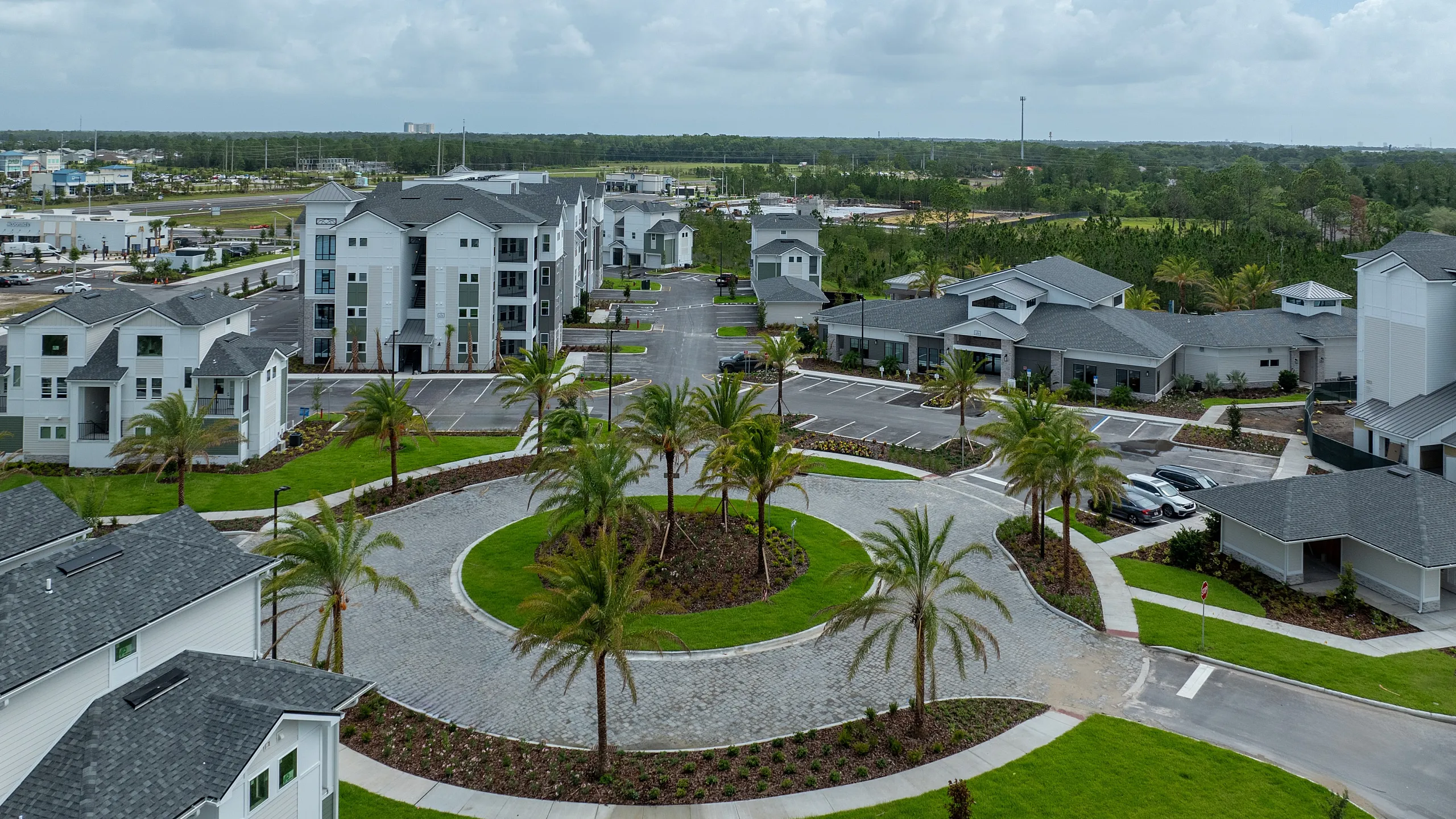 Beautiful aerial view of a modern apartment complex with lush green landscaping, palm trees, and spacious parking area on a sunny day.