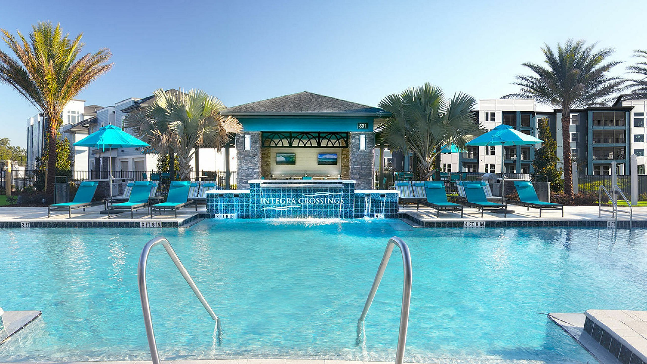 Luxurious pool area at Integra Crossings with turquoise loungers, palm trees, and modern apartments in the background, perfect for relaxation and leisure.