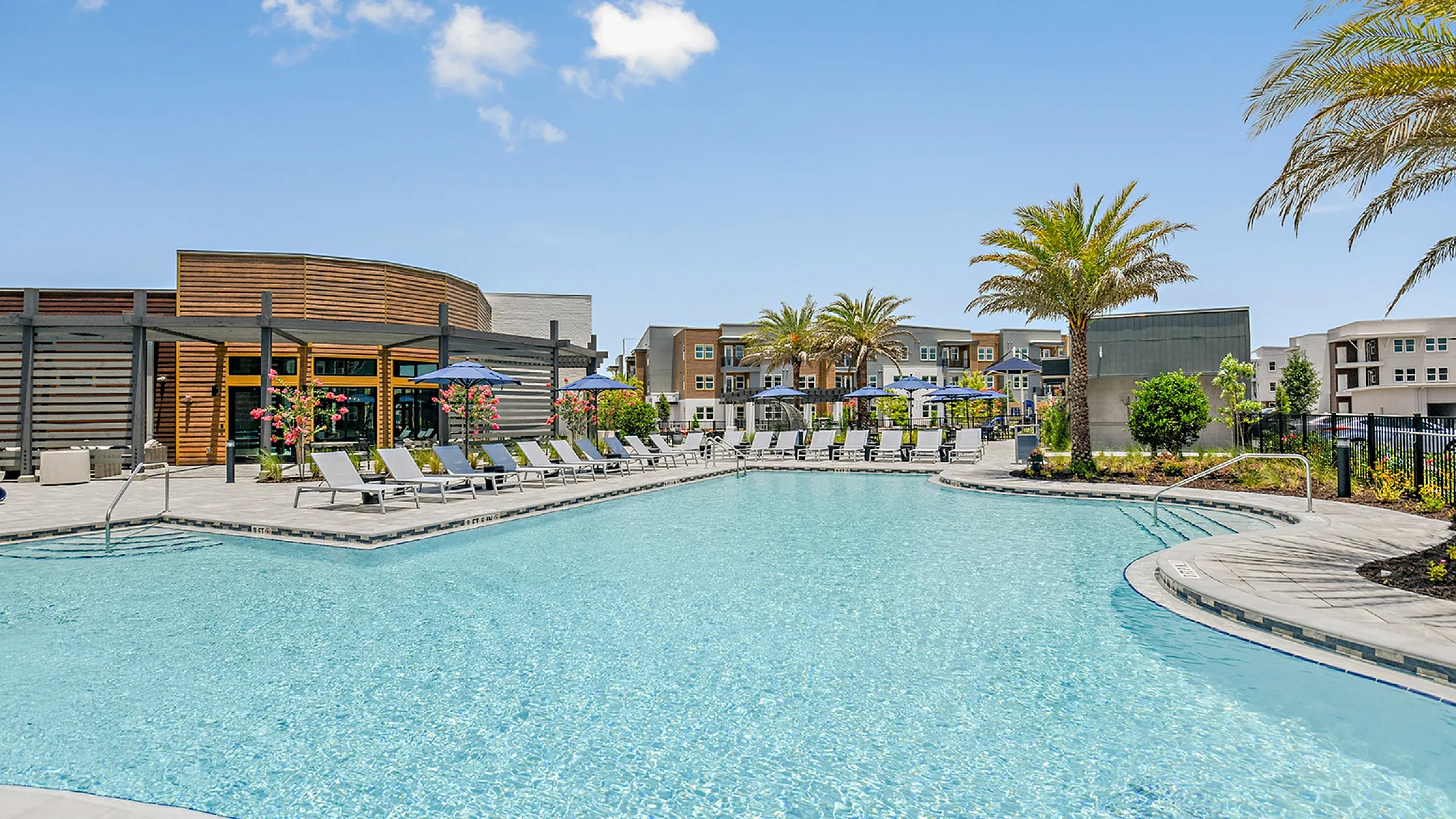 Luxurious apartment complex showcasing a sparkling resort-style pool surrounded by elegant loungers and tropical palm trees.