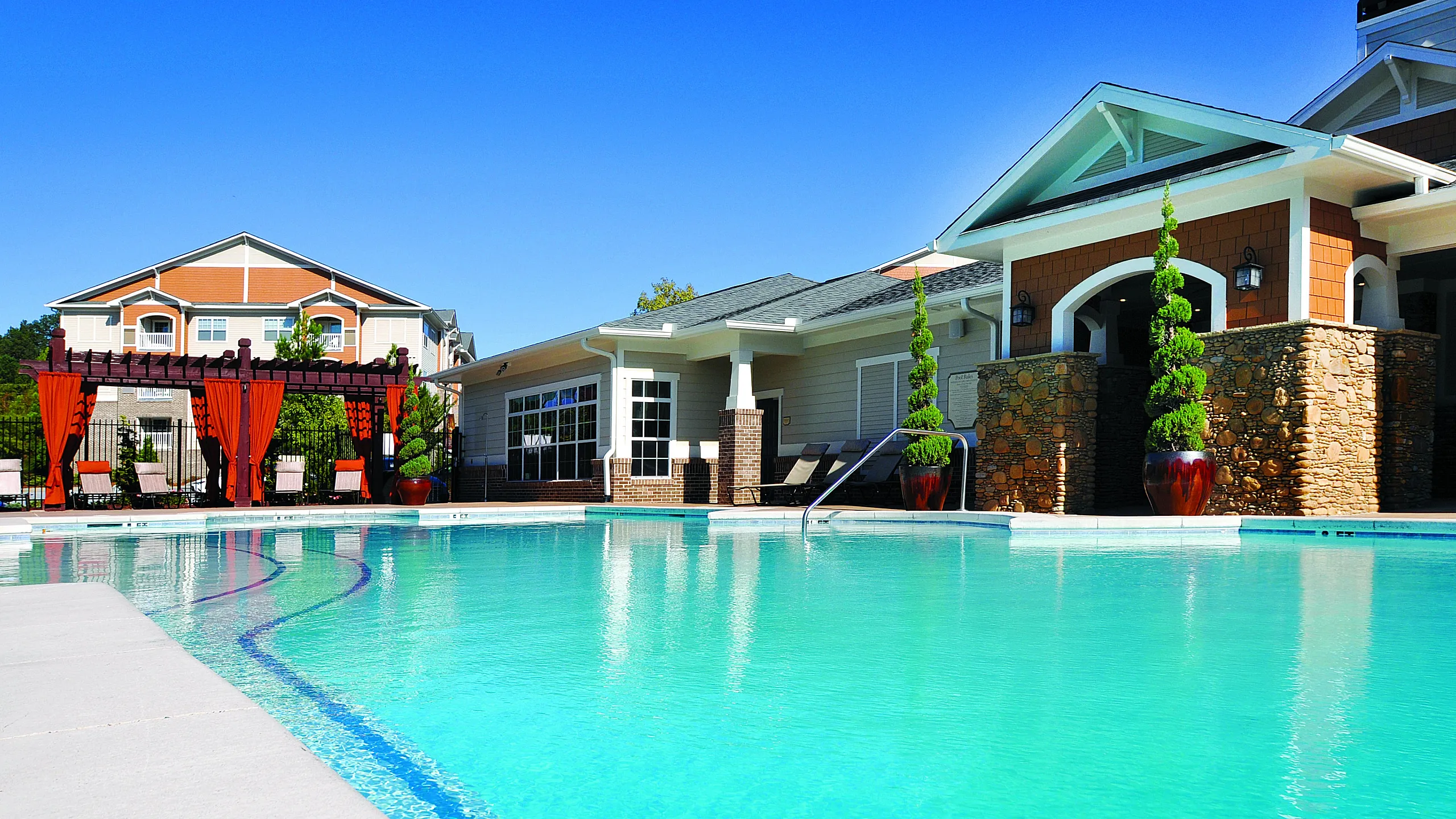 Luxurious apartment complex with a sparkling pool, elegant pergola area, and stylish architecture surrounded by lush greenery.