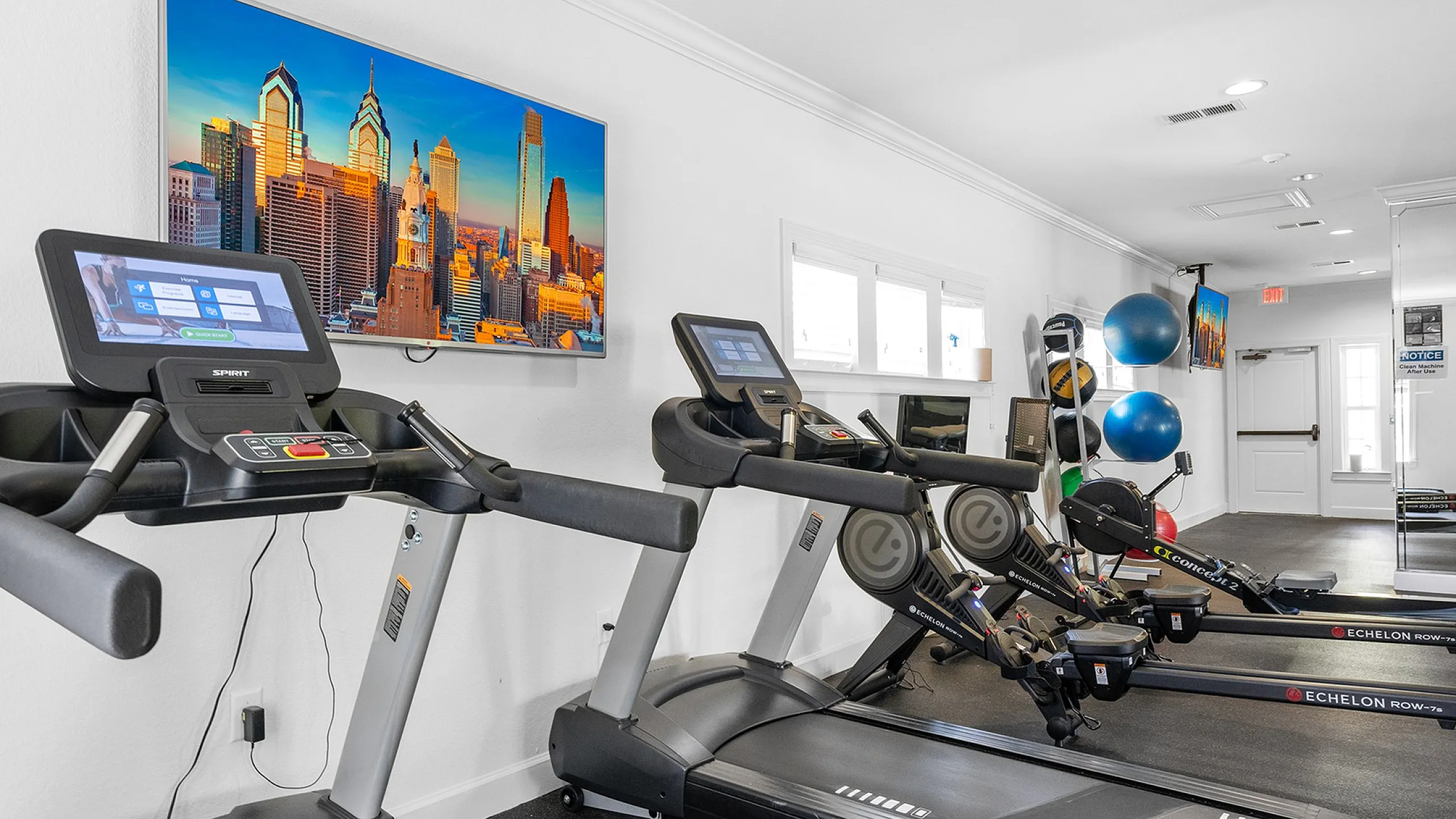 Modern apartment gym featuring state-of-the-art treadmills, rowing machines, and a vibrant city skyline photograph.