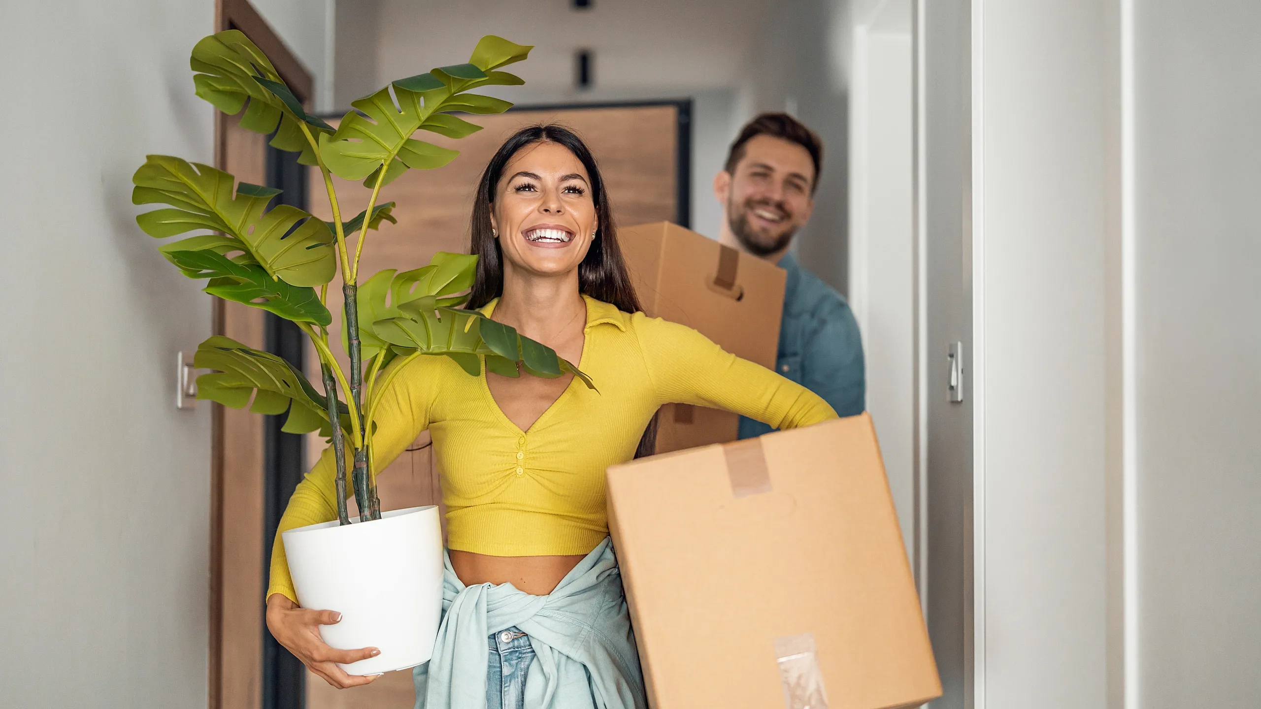 Happy couple moving into their new stylish apartment carrying boxes and a fresh green plant, radiating joy and excitement.