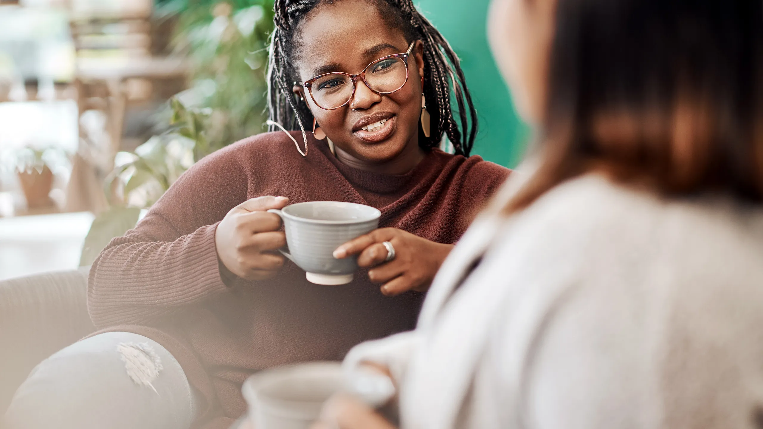 Warm and inviting setting with two people enjoying coffee and conversation, surrounded by lush greenery.