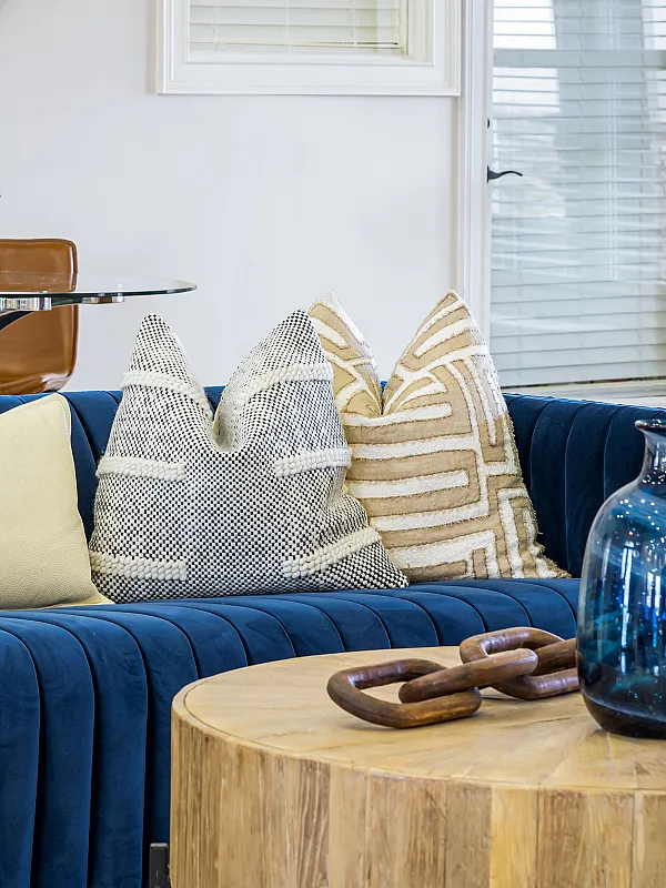 Chic living space featuring a plush blue sofa with decorative pillows, a stylish wooden coffee table, and a glass dining area with elegant leather chairs.