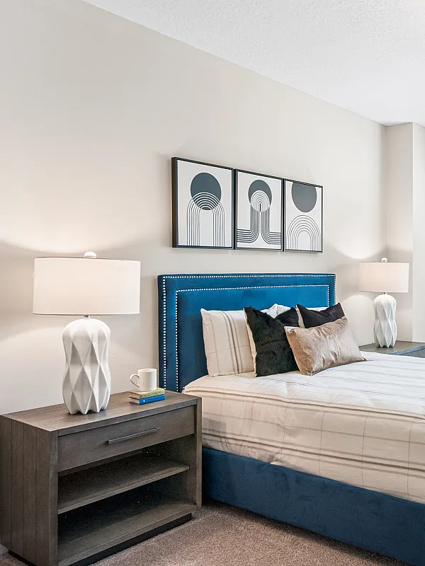 Bright and inviting bedroom with plush blue bed, modern decor, and large window offering plenty of natural light.