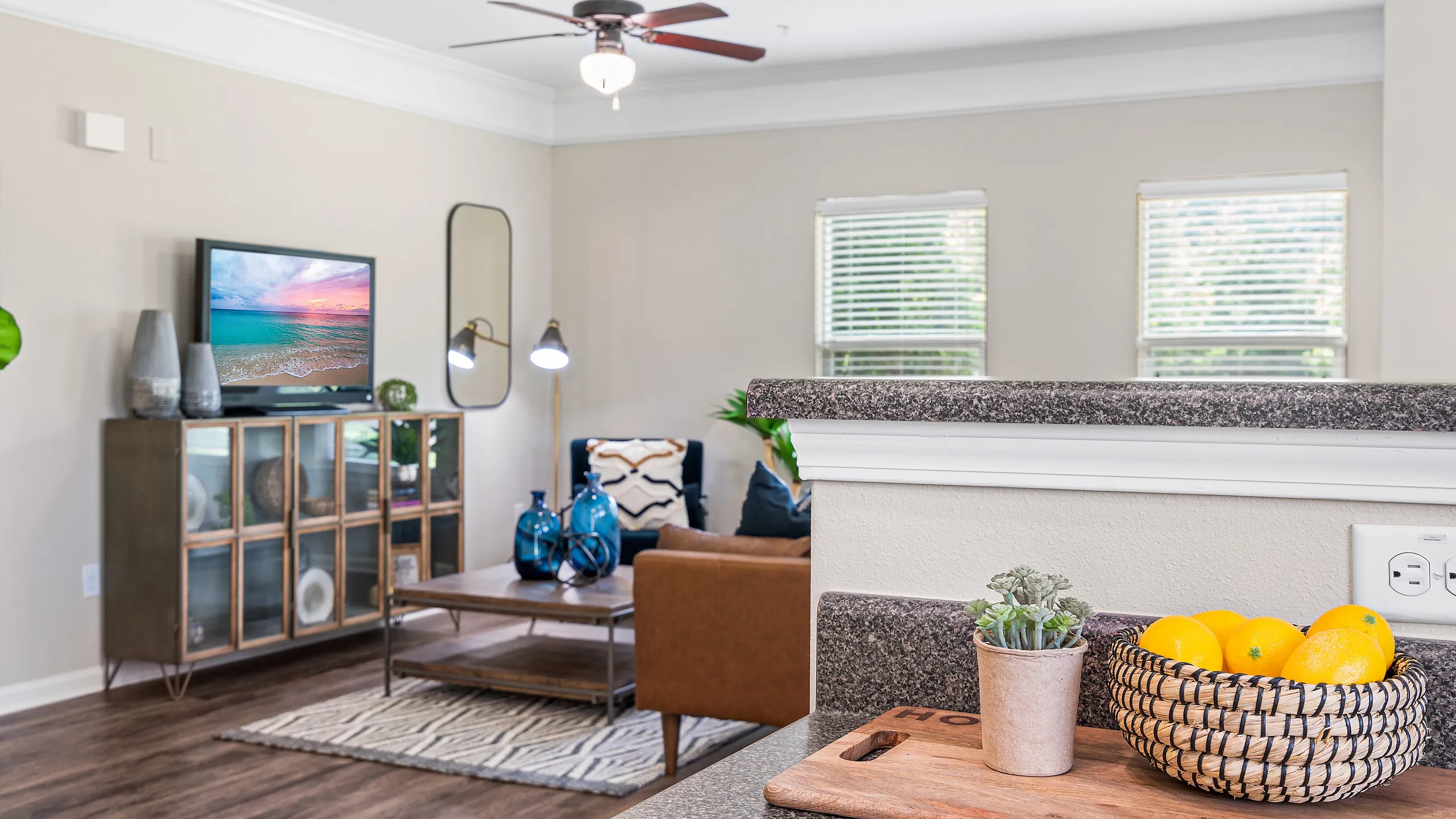 Inviting living room with modern decor, featuring a cozy armchair, vibrant blue vases, and a wall-mounted TV beneath a ceiling fan.