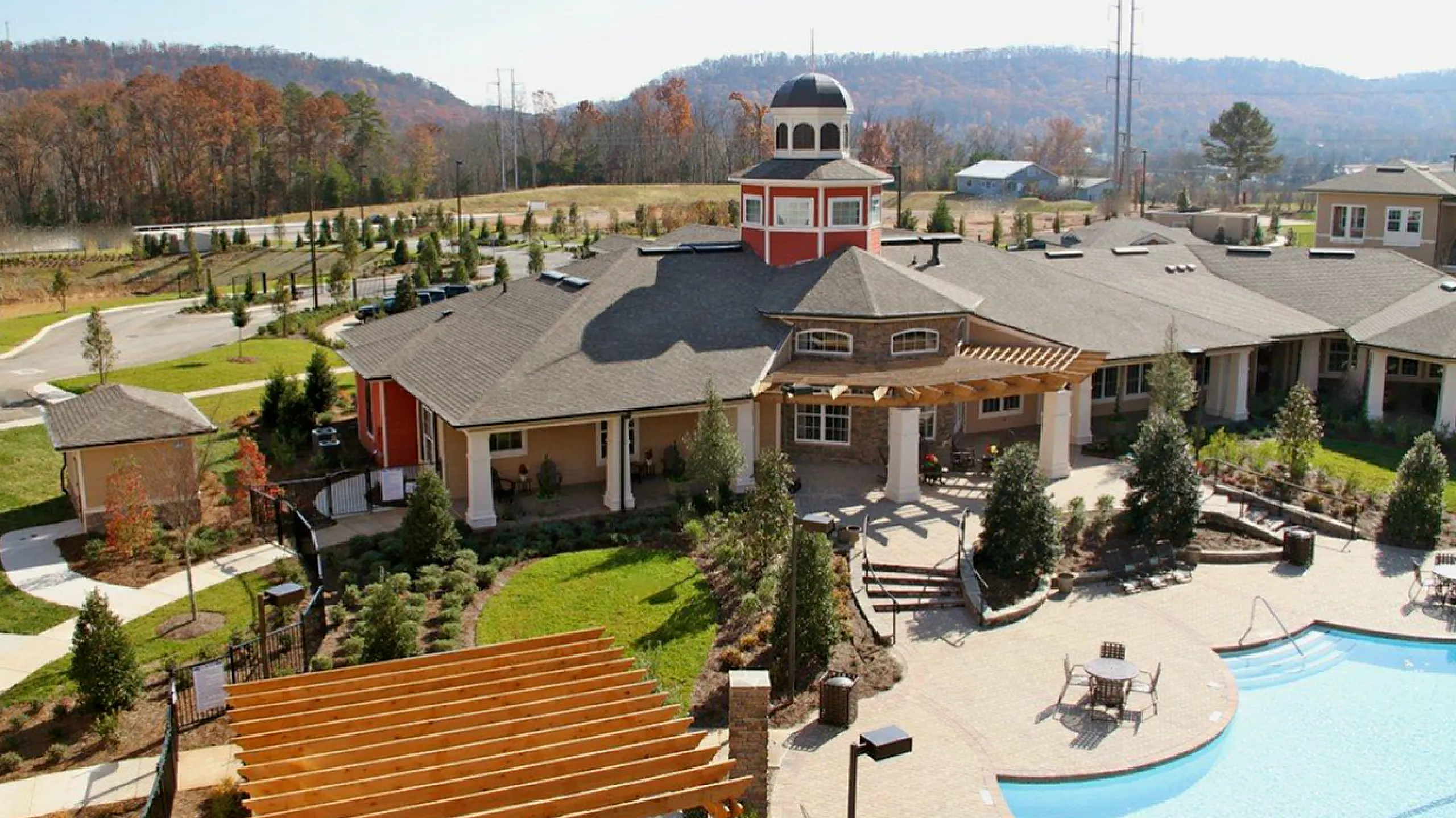 Scenic view of a luxurious apartment complex with a spacious courtyard, inviting pool, and picturesque mountain backdrop.