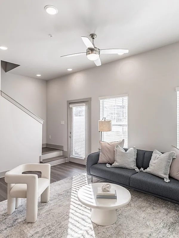 Bright and modern living room with neutral decor, featuring a plush sofa, chic armchair, and stylish coffee table under a sleek ceiling fan.