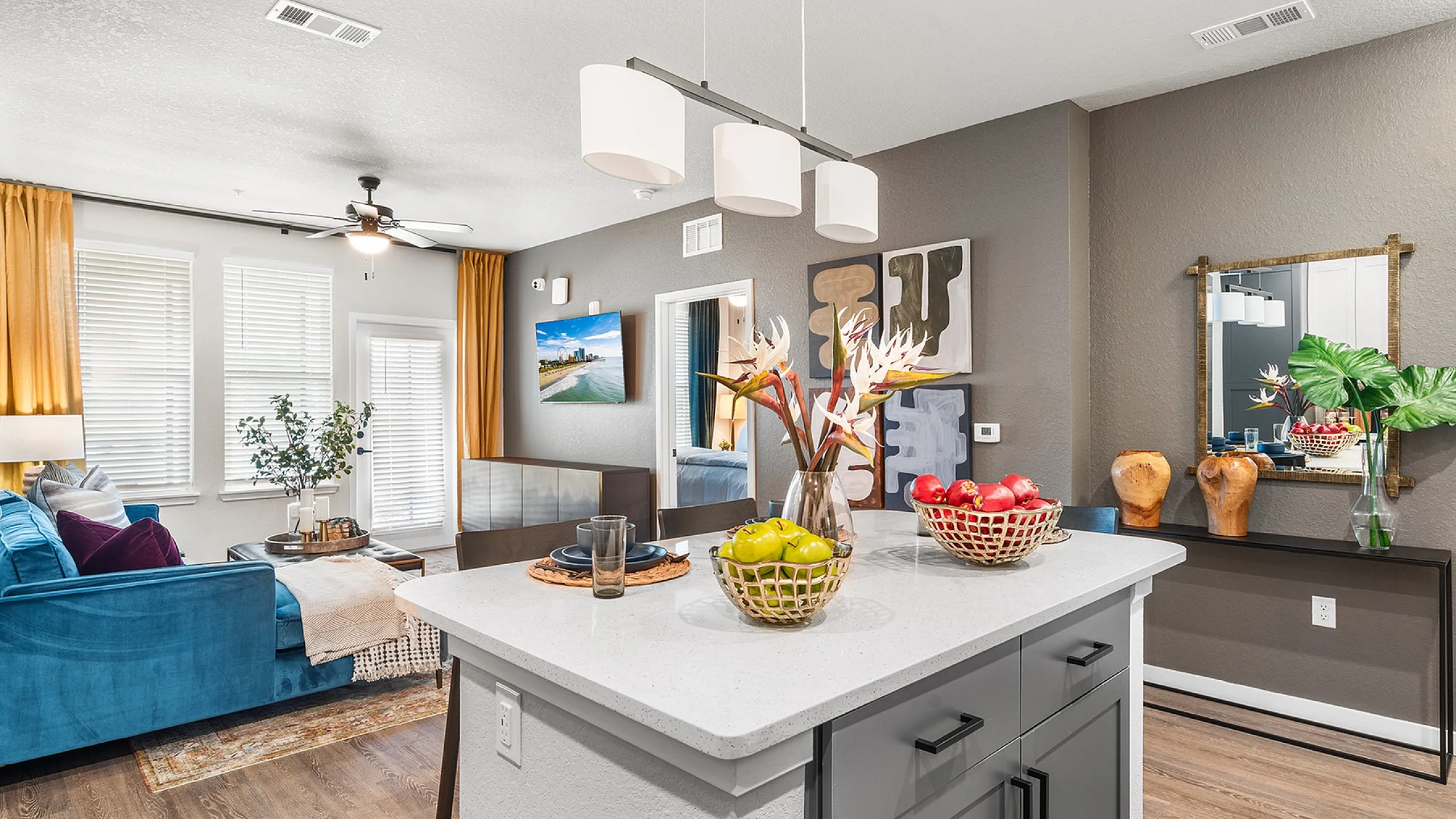 Stylish open-concept living room with vibrant blue sofa, modern kitchen island with fruit bowls, and elegant decor.