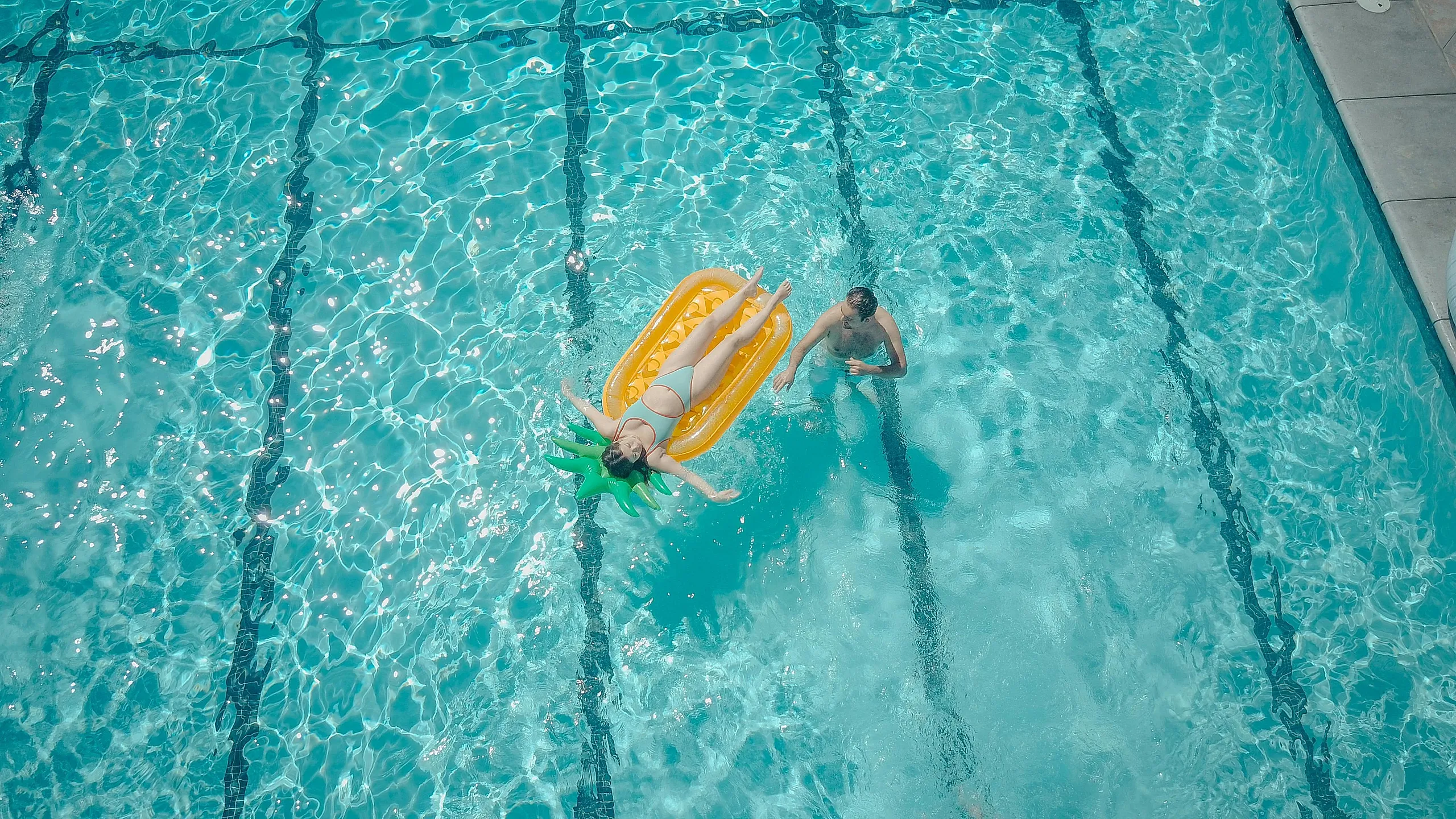 Inviting swimming pool with a relaxing atmosphere, featuring a person lounging on a vibrant float and another enjoying the crystal-clear water.