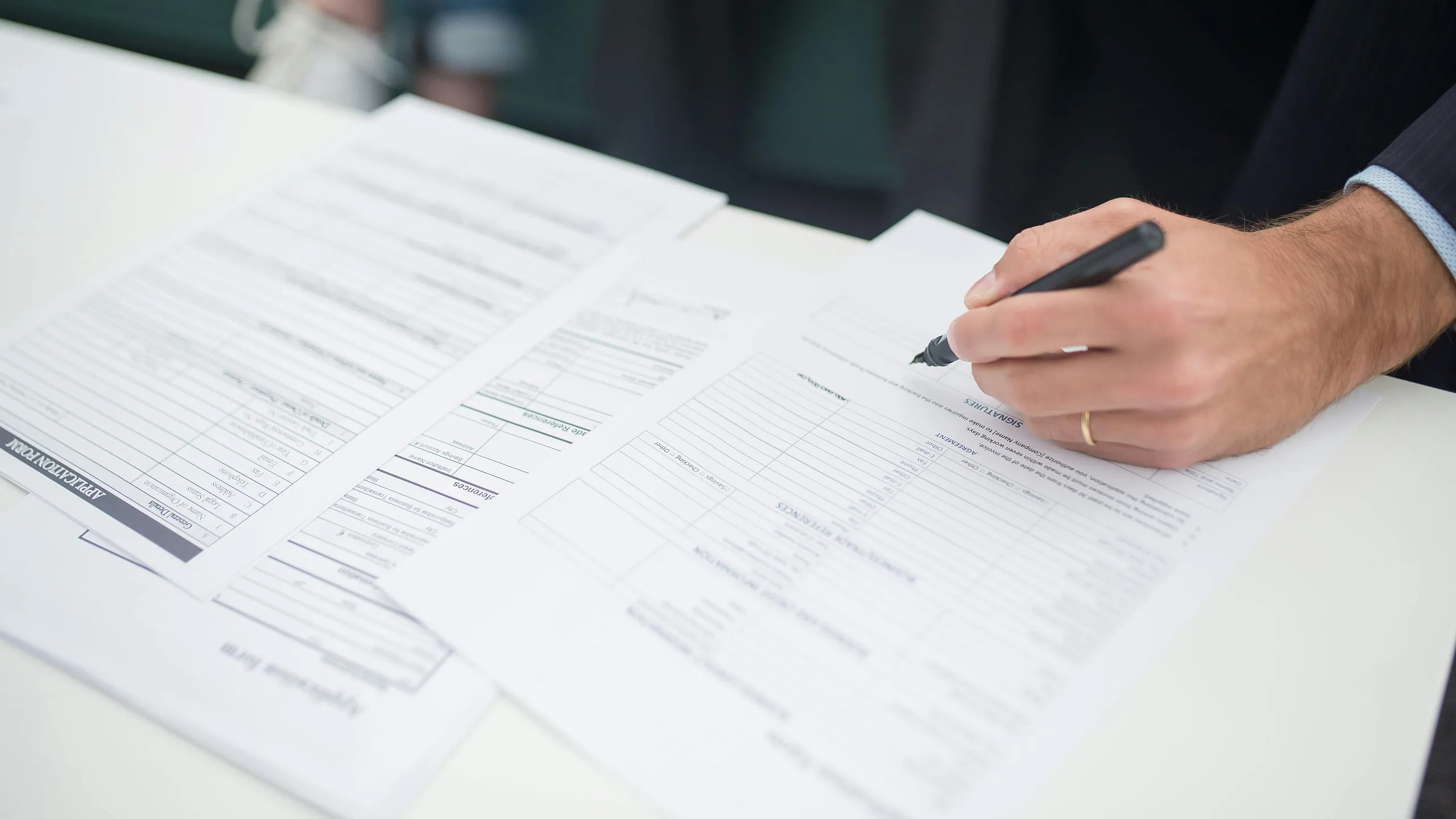 Person confidently signing document on a bright white desk, featuring detailed forms and organized paperwork.