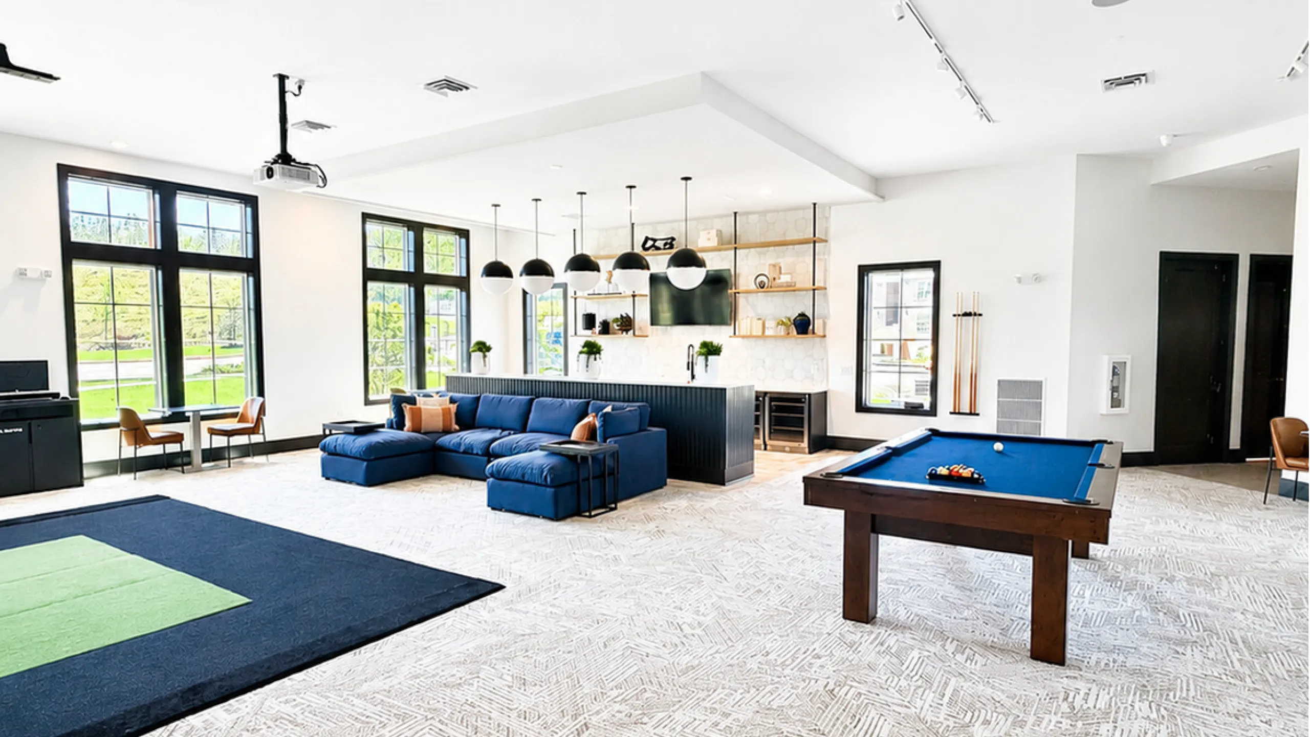Modern and spacious living area featuring a sleek blue sofa, stylish pool table, and an elegant kitchen with pendant lighting.