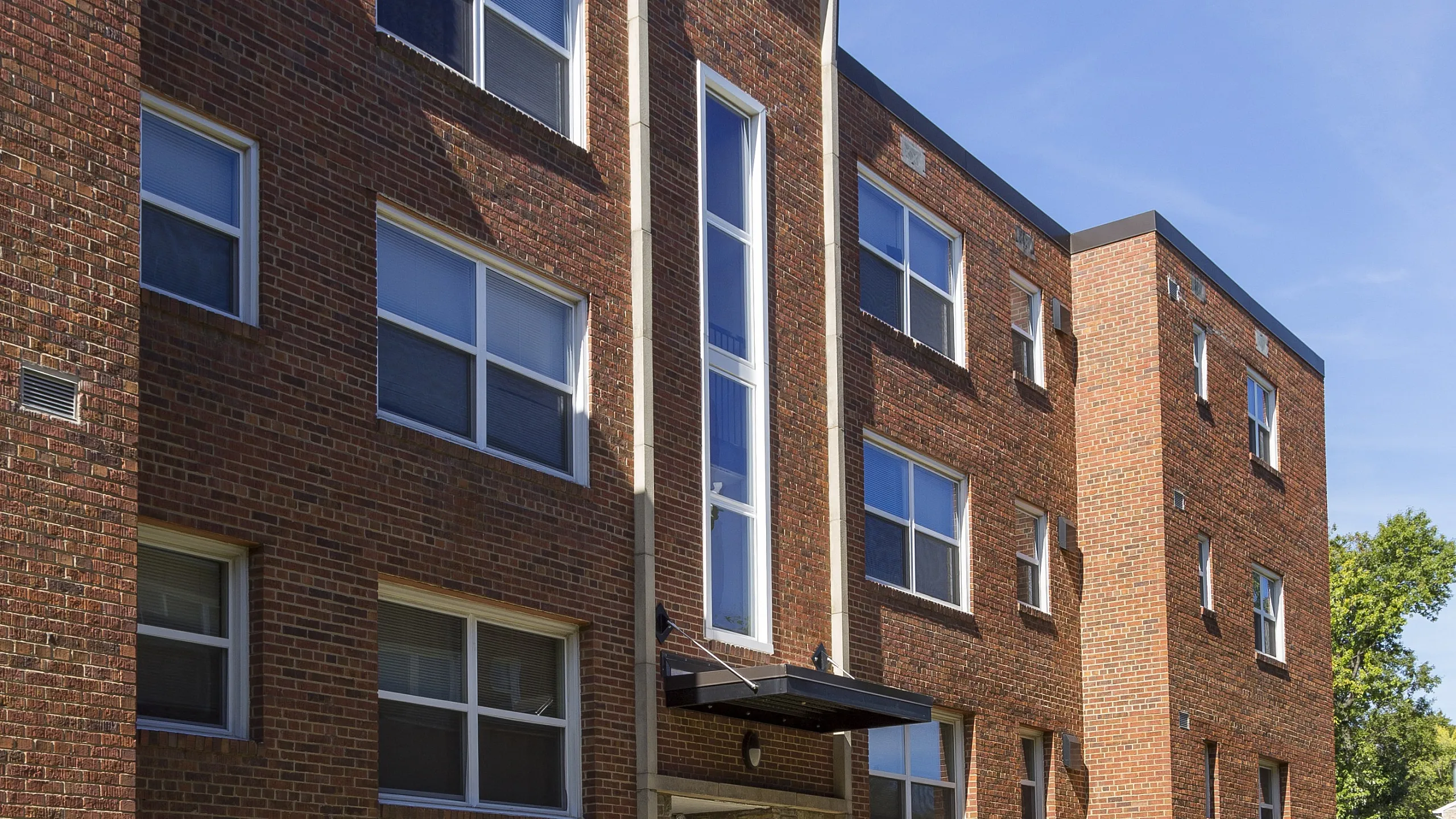 Charming brick apartment building with modern windows and a well-maintained lawn under a bright blue sky.