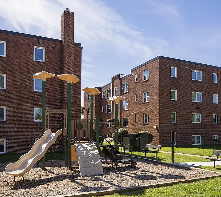 Charming brick apartment buildings with a sunny outdoor playground, perfect for family living.