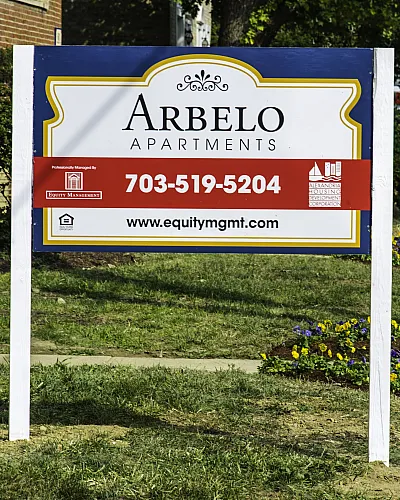 Inviting Arbelo Apartments sign displaying contact information, set against a charming neighborhood backdrop with vibrant flowers.