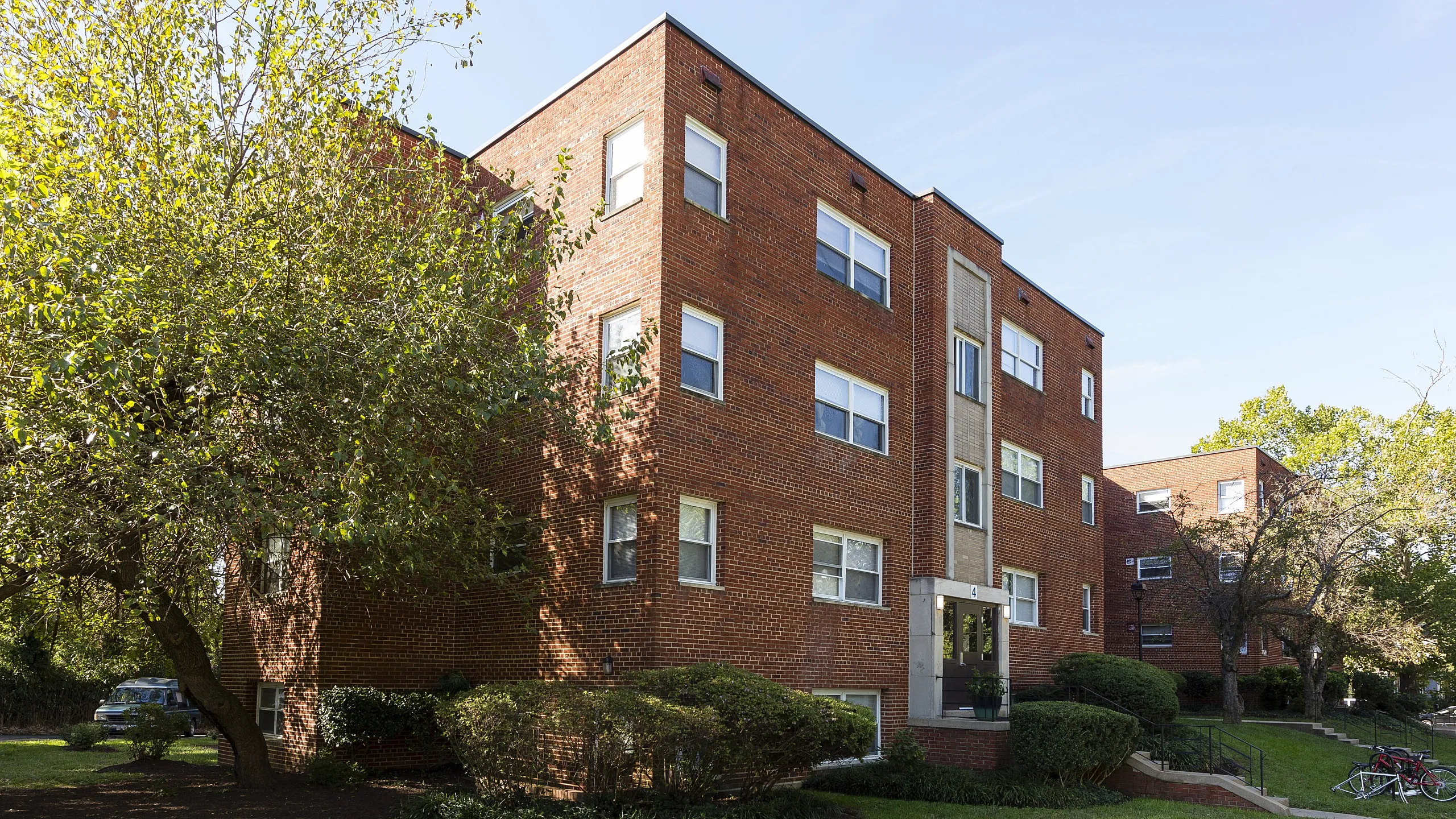 Charming red-brick apartment building with lush green landscaping and a welcoming entrance.