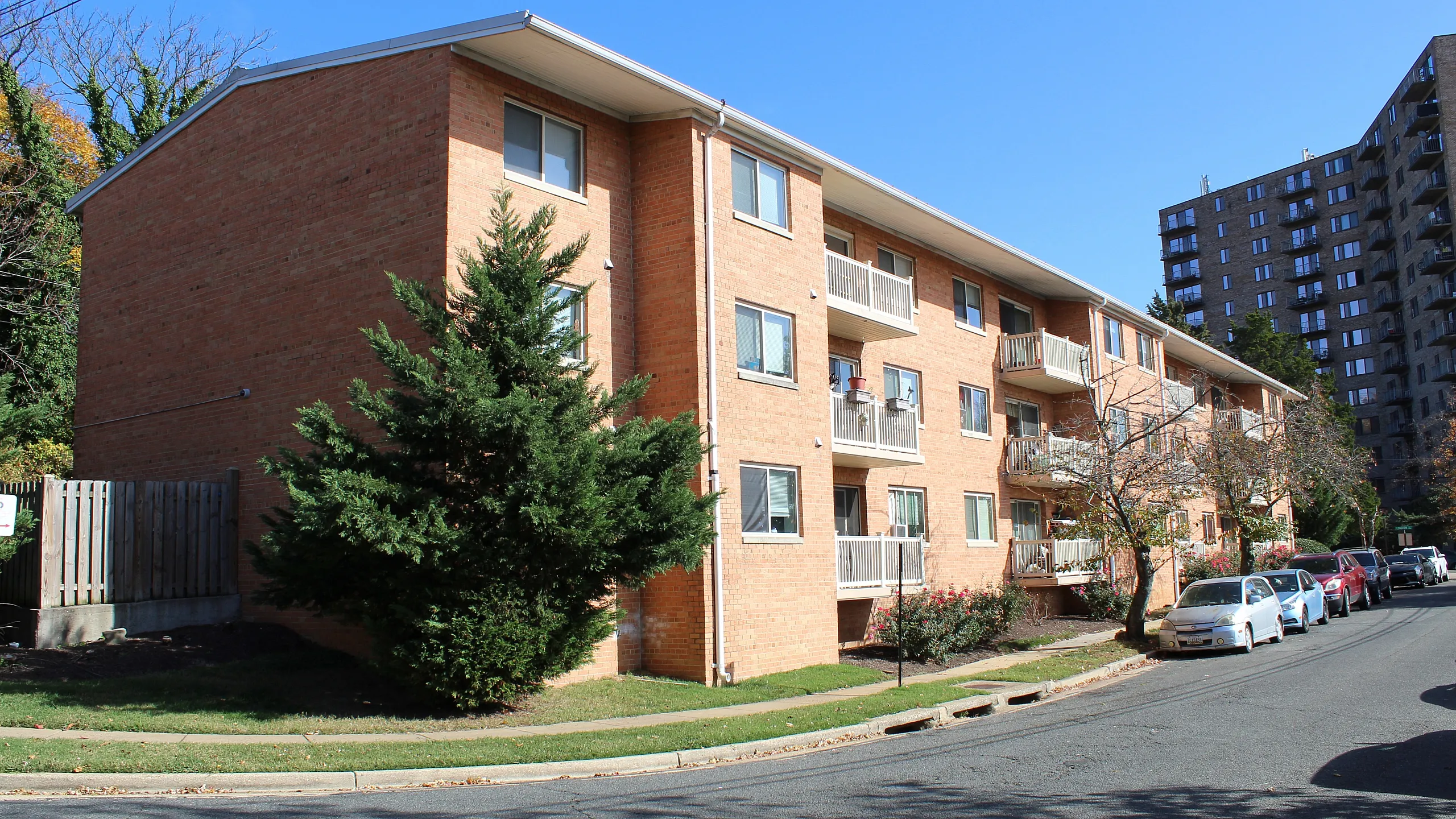 Charming brick apartment building with balconies and lush landscaping on a sunny day.