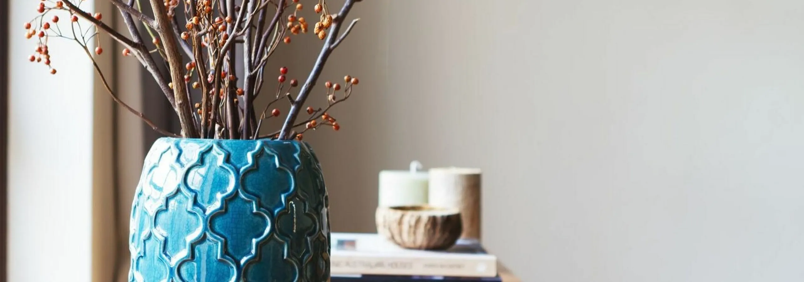 Elegant teal vase with intricate patterns, adorned with delicate branches on a stylish wooden table, creating a modern and inviting atmosphere.