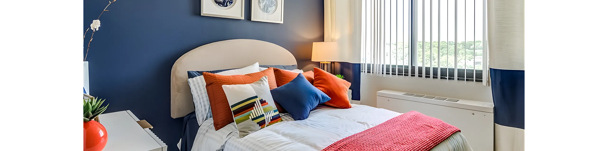Inviting contemporary bedroom with a navy blue accent wall, vibrant pillows, and a sunlit window.