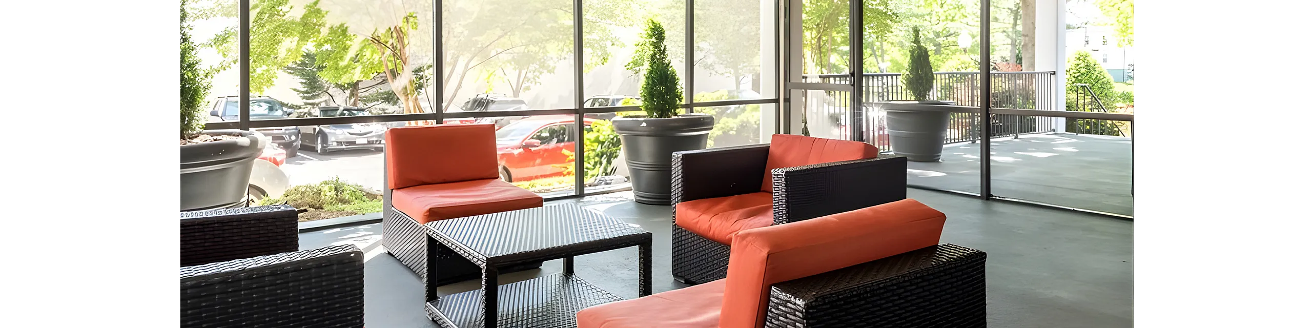 Chic sunlit lounge area with modern wicker furniture and vibrant orange cushions, seamlessly connecting with the outdoor greenery through floor-to-ceiling windows.