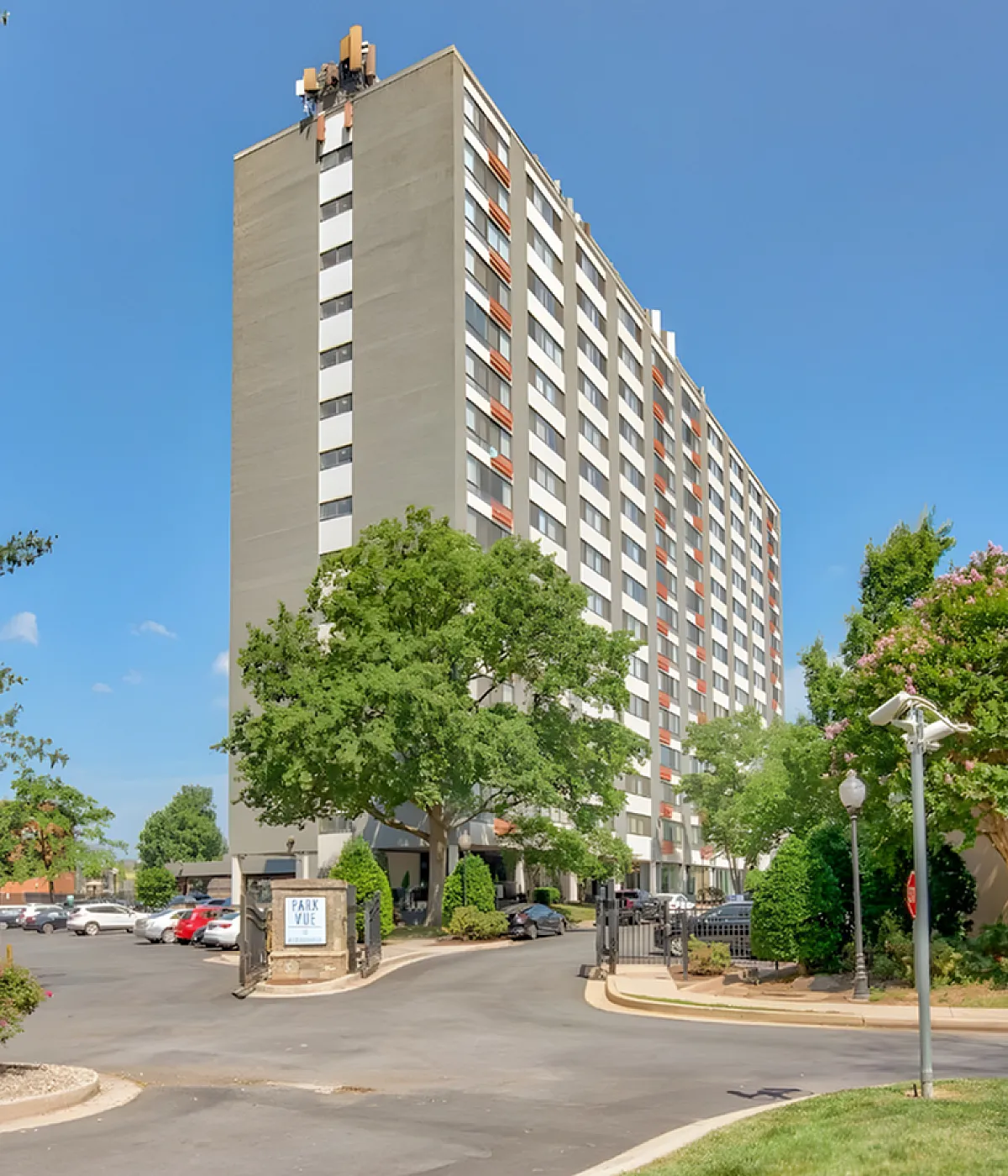 Inviting high-rise apartment building surrounded by lush greenery and a bright blue sky, offering modern urban living with convenient access and scenic views.