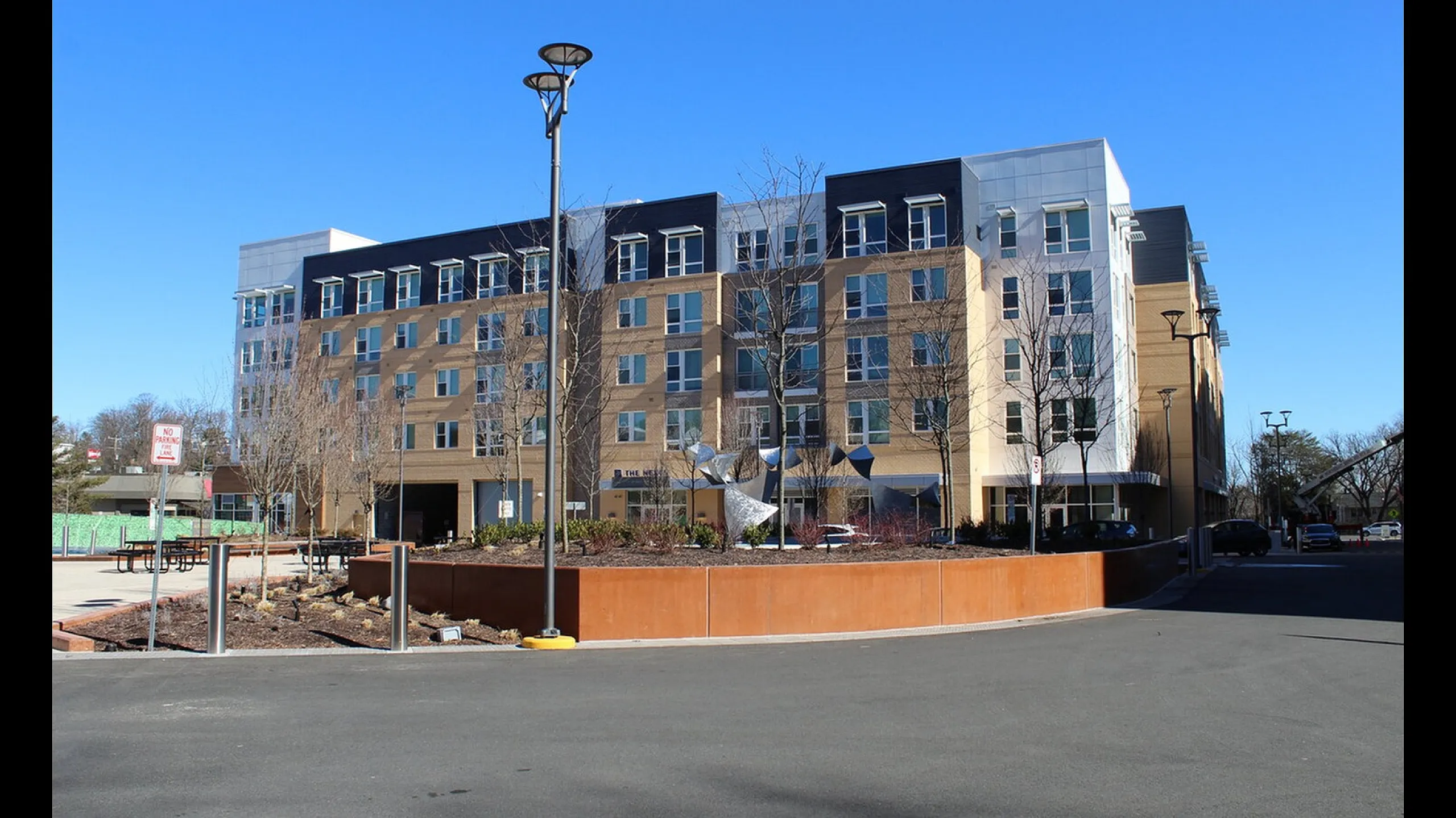 Modern apartment building with stylish architecture, featuring large windows and attractive landscaping under a clear blue sky.