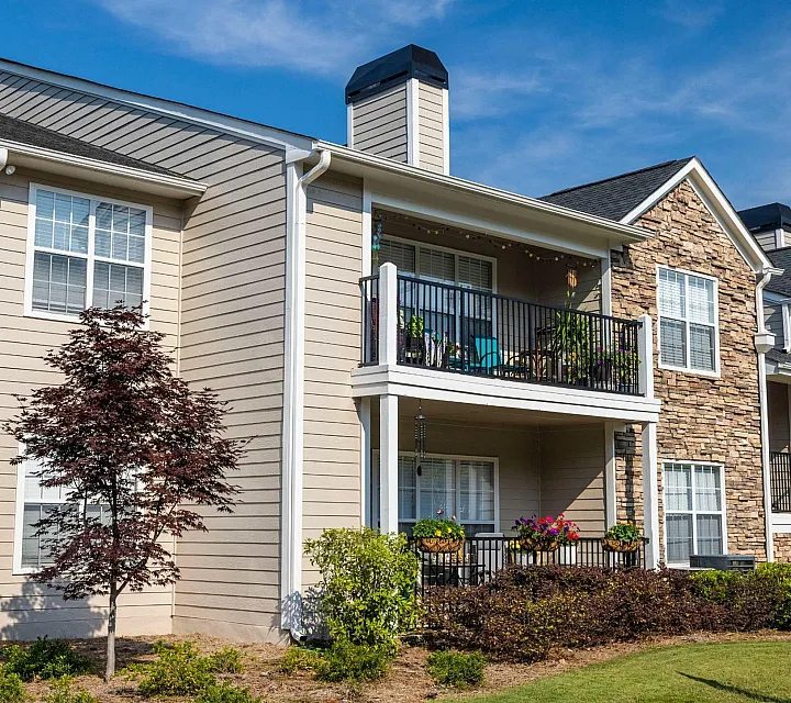Beautiful suburban apartment complex with balconies, a lush lawn, and vibrant plants under a clear blue sky.