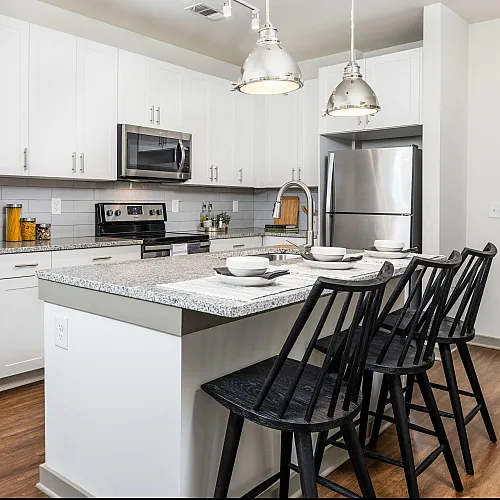 Modern kitchen with white cabinets, granite countertops, stainless steel appliances, and stylish bar seating.