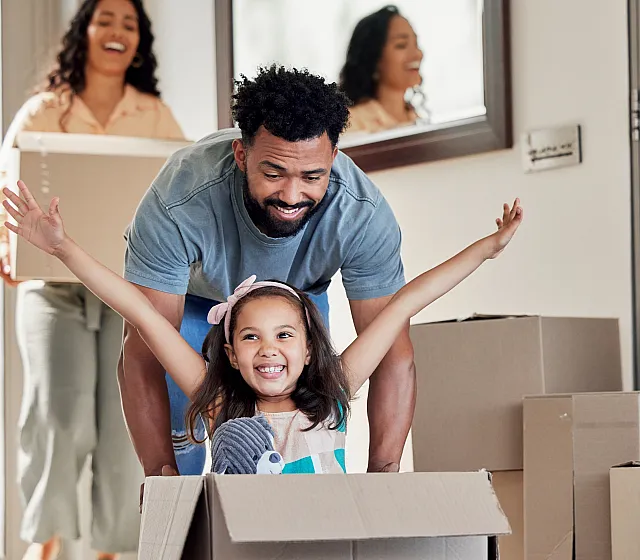 Joyful family moving into a new home, surrounded by boxes, with a child playing in a box.