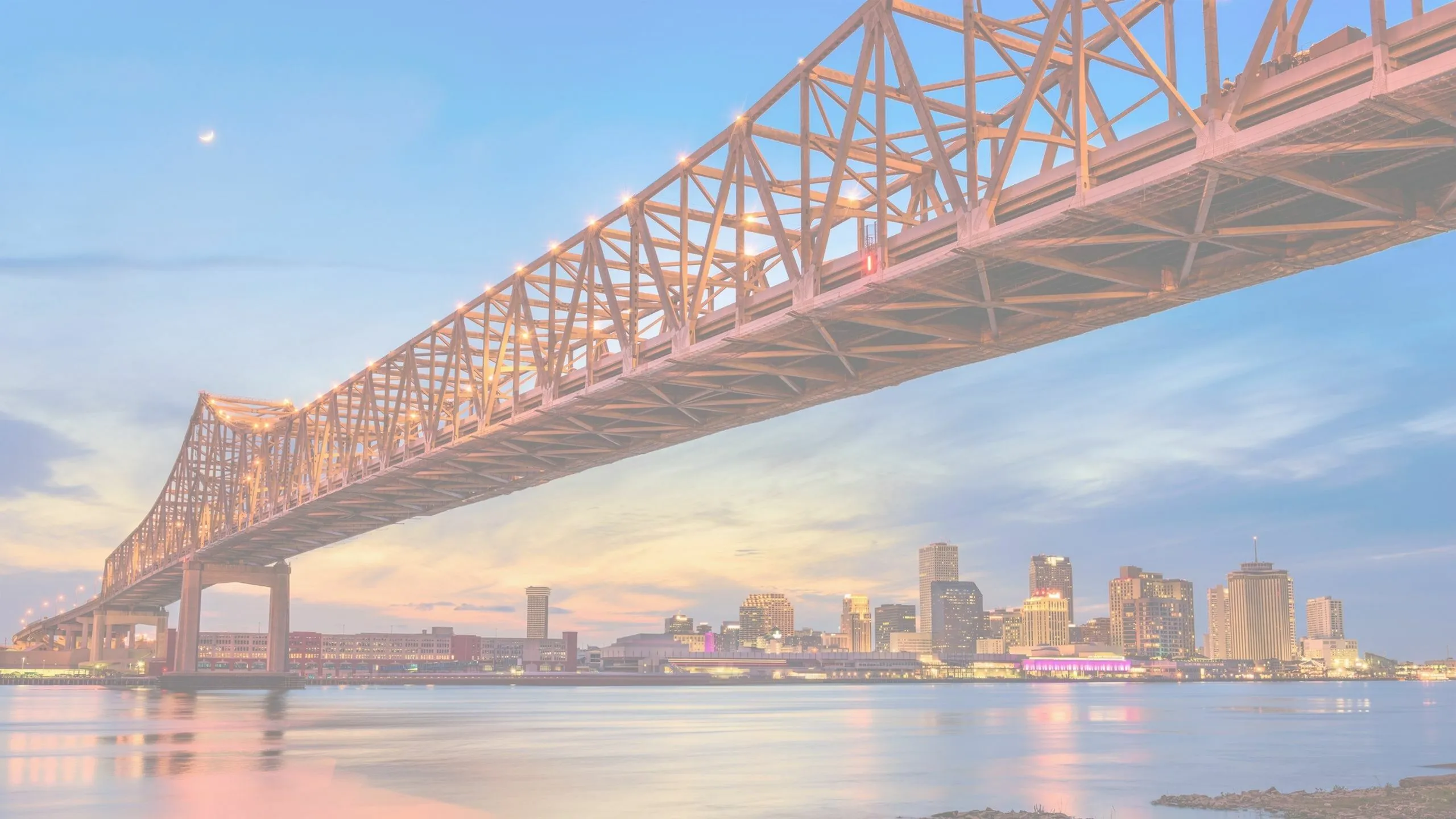 Stunning view of a large bridge spanning over a calm river with a vibrant city skyline at dusk.