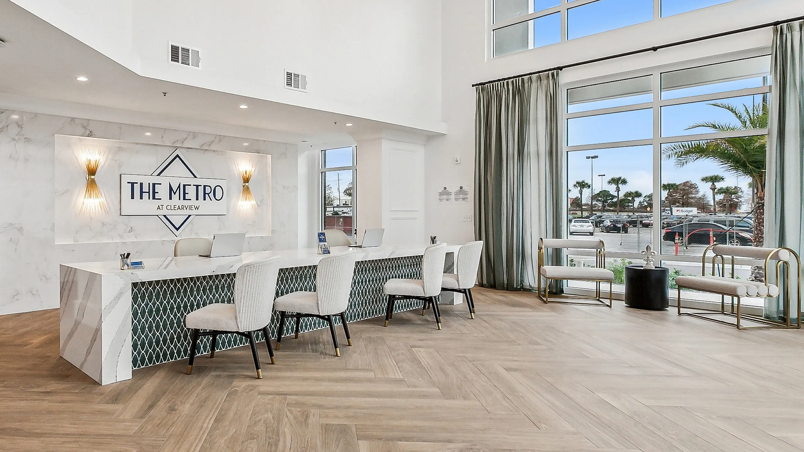 Luxurious lobby of The Metro at Clearview with elegant chandelier lighting, modern reception desk, and large sunlit windows overlooking palm trees.
