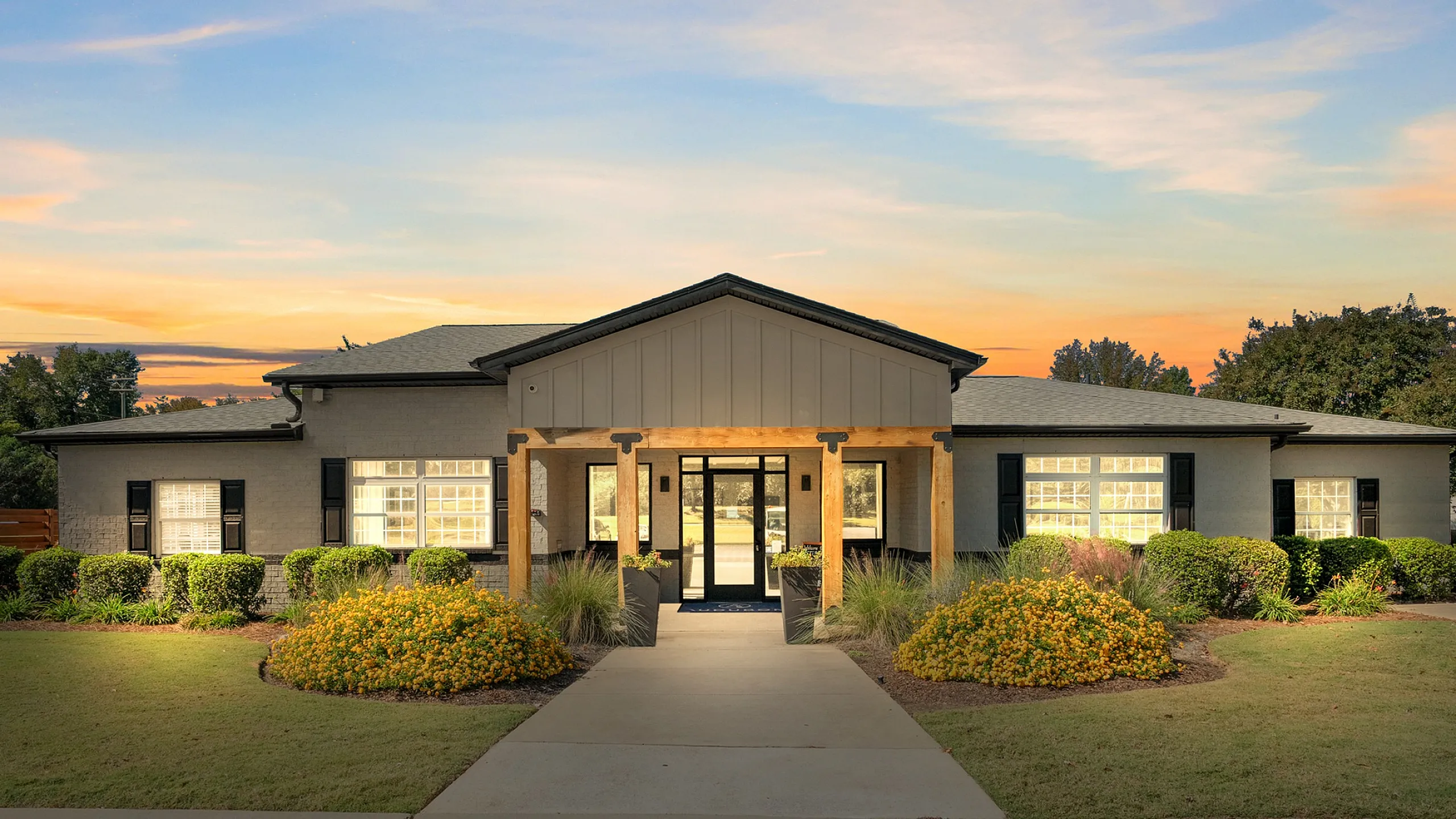Charming community entrance with lush landscaping and welcoming pathway under a colorful sunset.