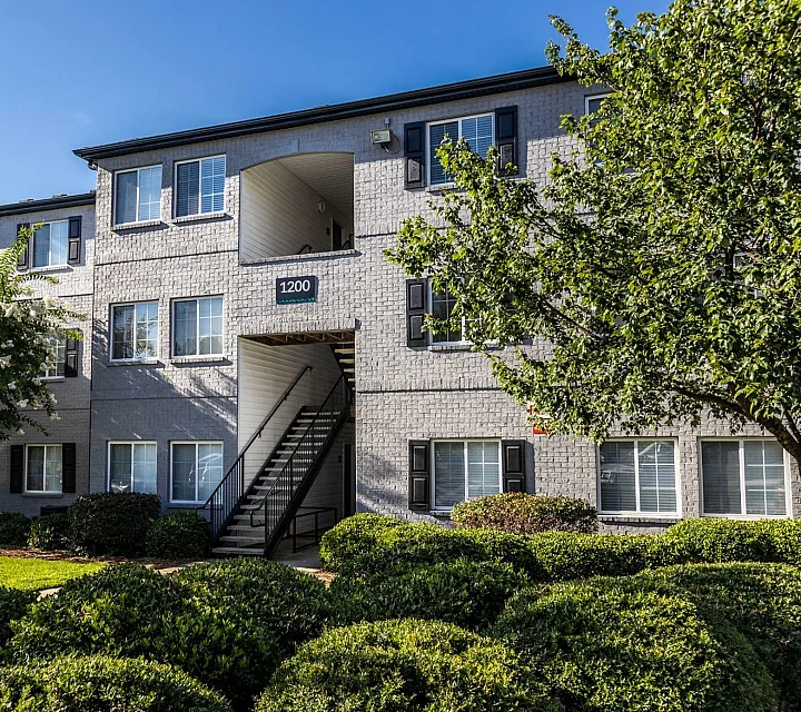 Charming brick apartment building with manicured landscaping against a clear blue sky.