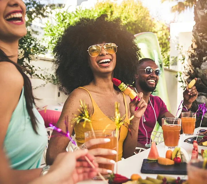Joyful friends enjoying a vibrant outdoor gathering with delicious fruit platters and colorful drinks.