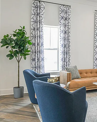 Bright and stylish living room featuring a contemporary leather sofa, chic blue armchairs, and elegant patterned curtains, with abundant natural light and modern decor accents.