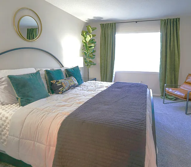 Luxurious bedroom with a stylish king-sized bed adorned with plush pillows, complemented by a sleek leather chair and lush greenery, all basking in natural light.