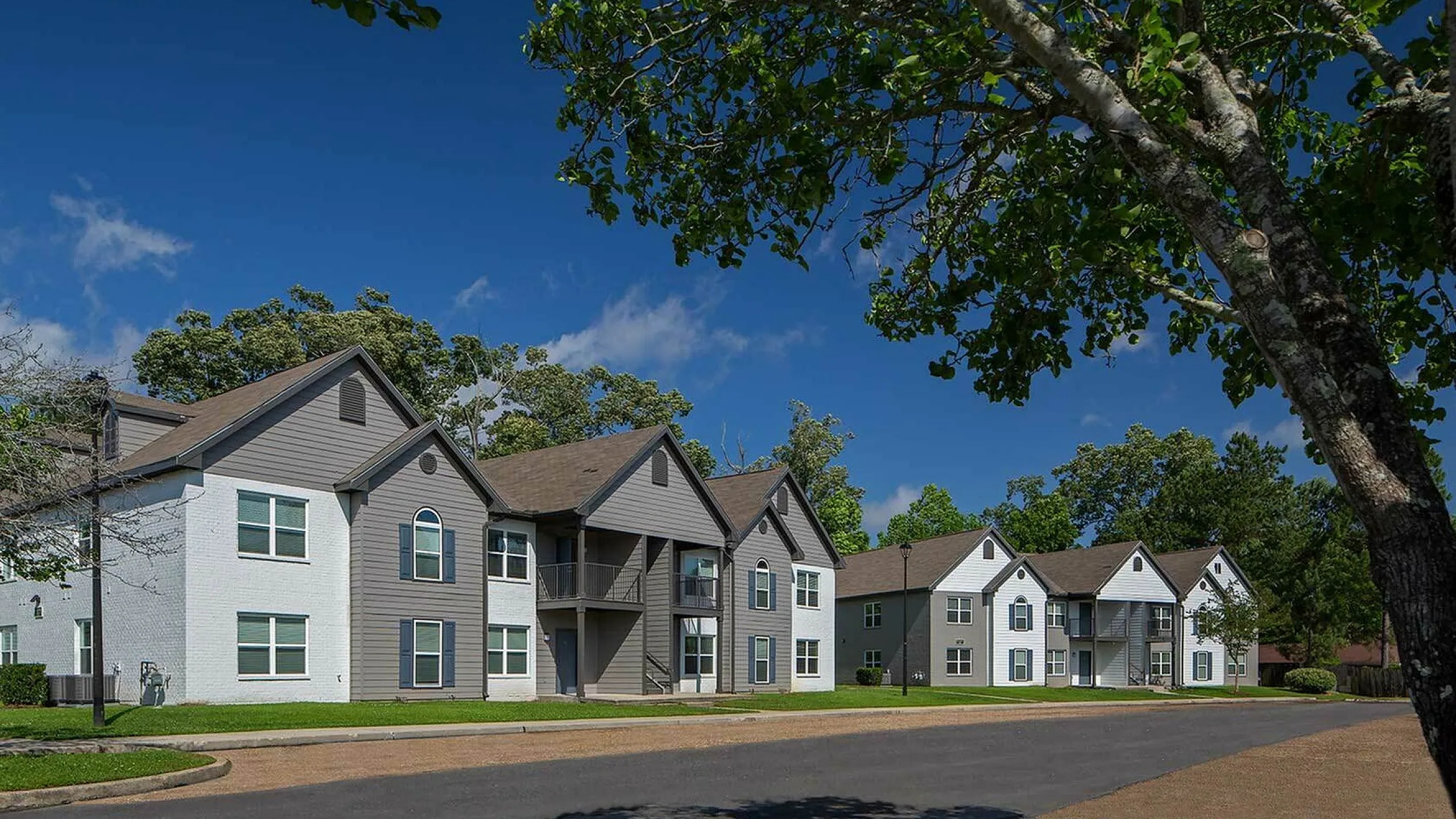 Charming apartment complex with modern architecture, nestled among lush greenery under a clear blue sky.