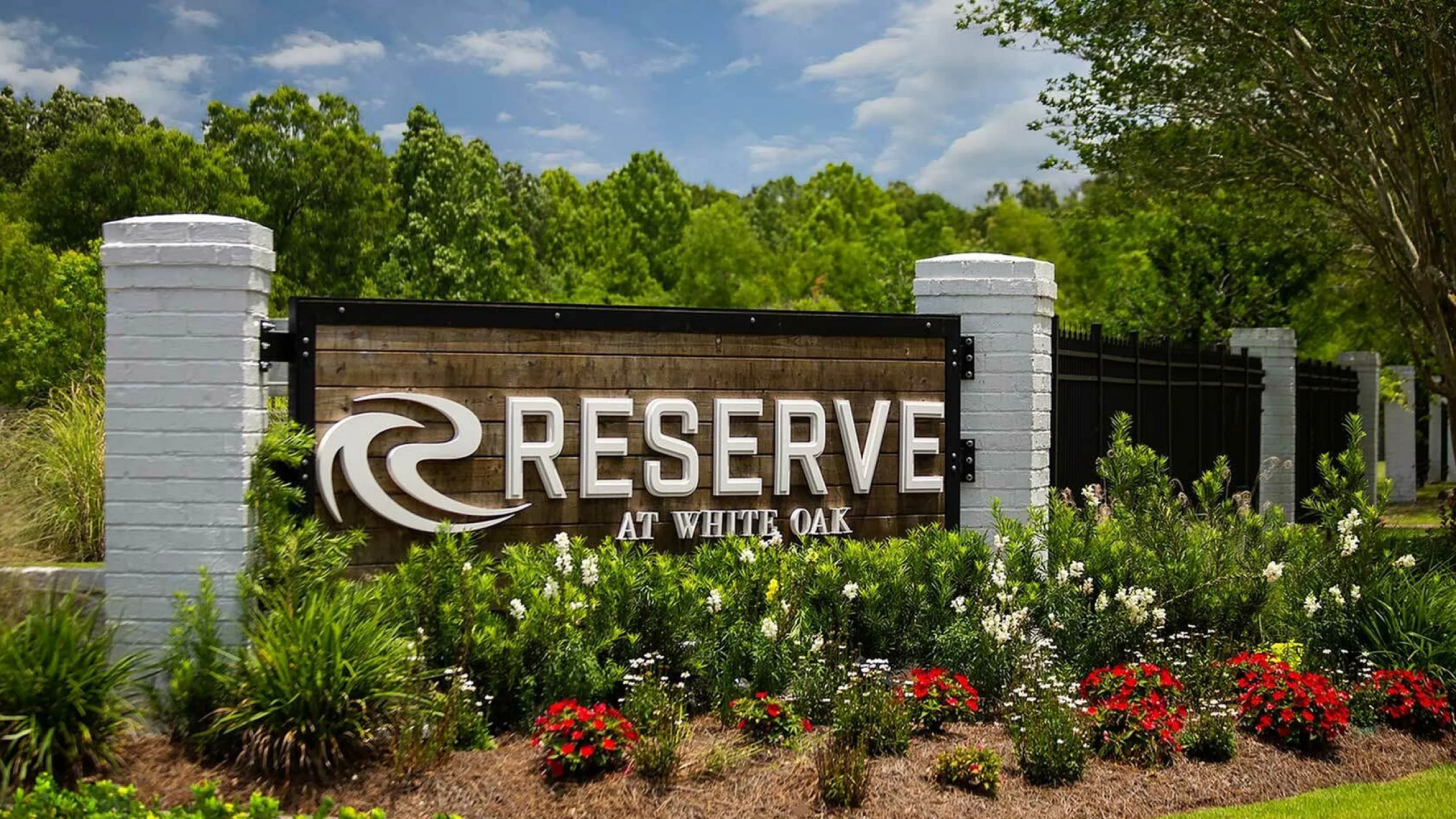 Welcoming entrance sign of Reserve at White Oak, surrounded by lush greenery and vibrant flowers.