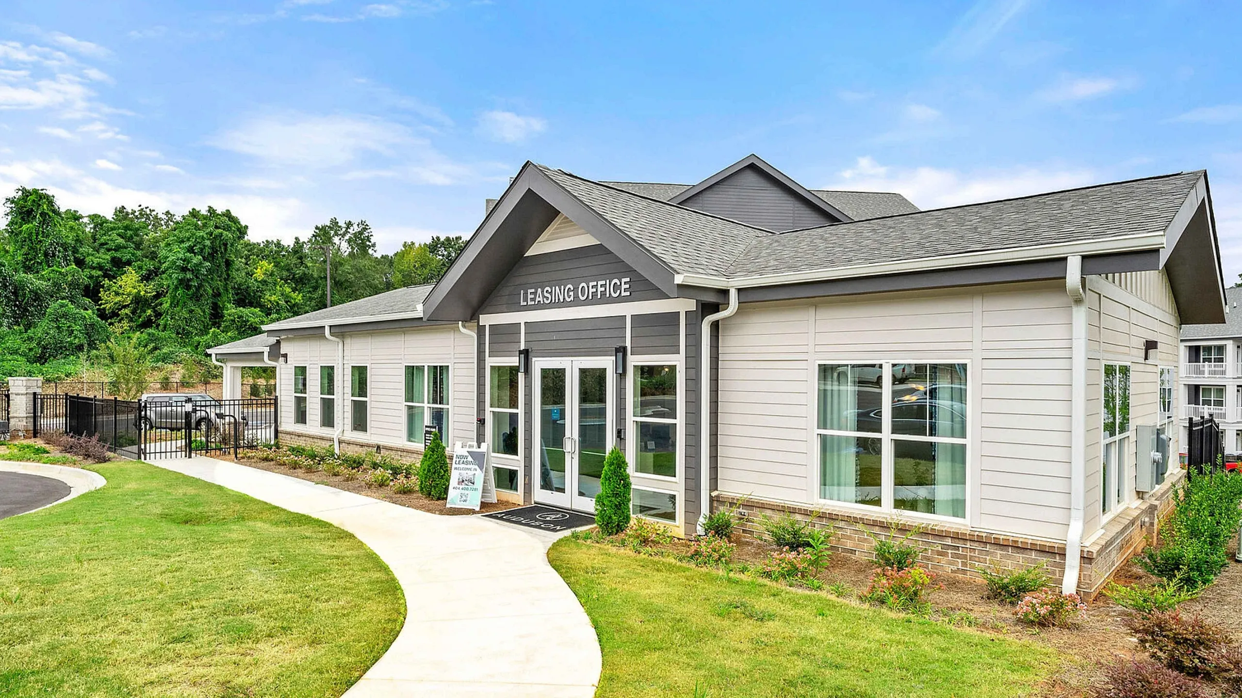 Inviting leasing office with modern architecture, surrounded by lush greenery and a welcoming pathway.